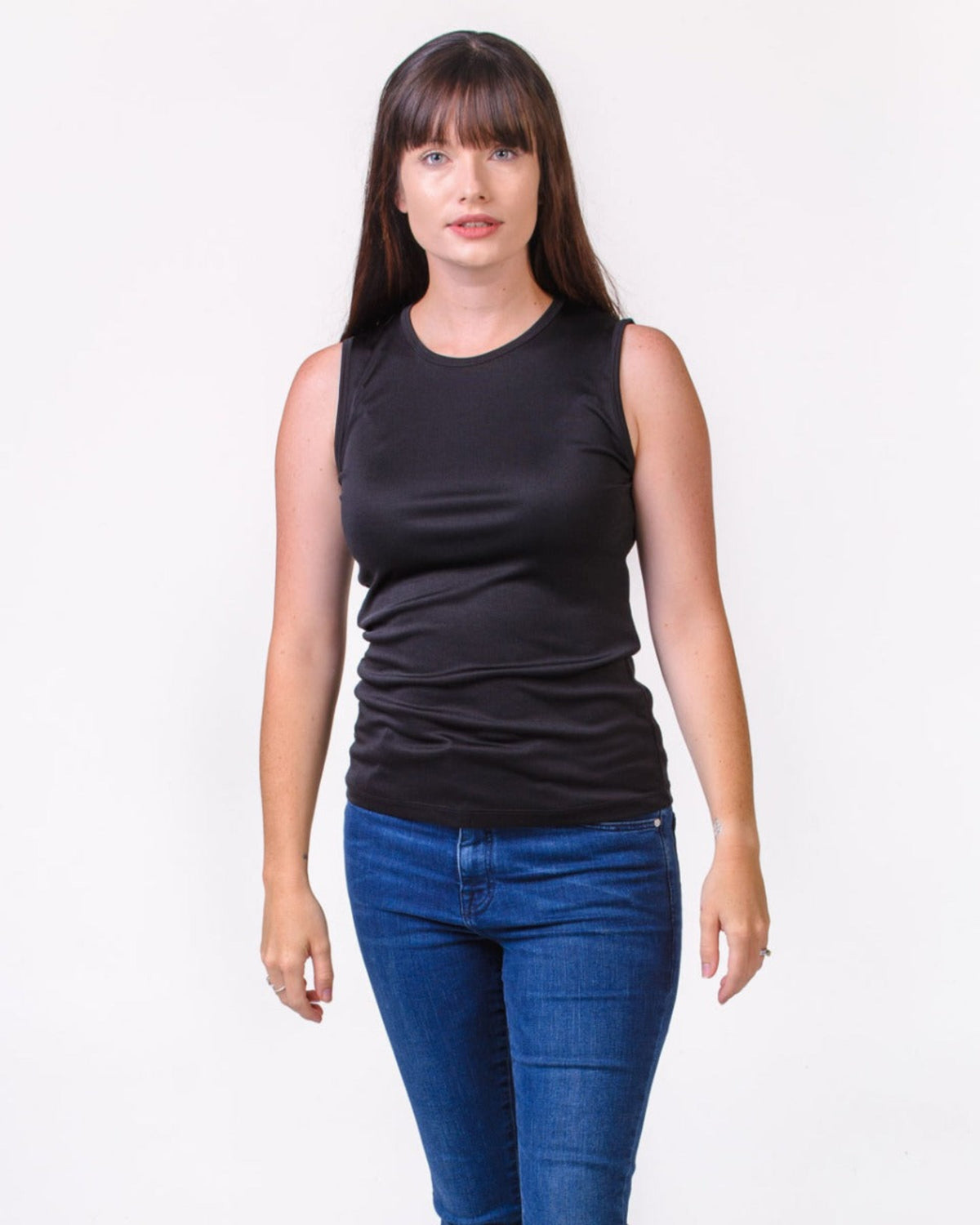 Woman wearing a silk  black sleeveless top and blue jeans on a white background