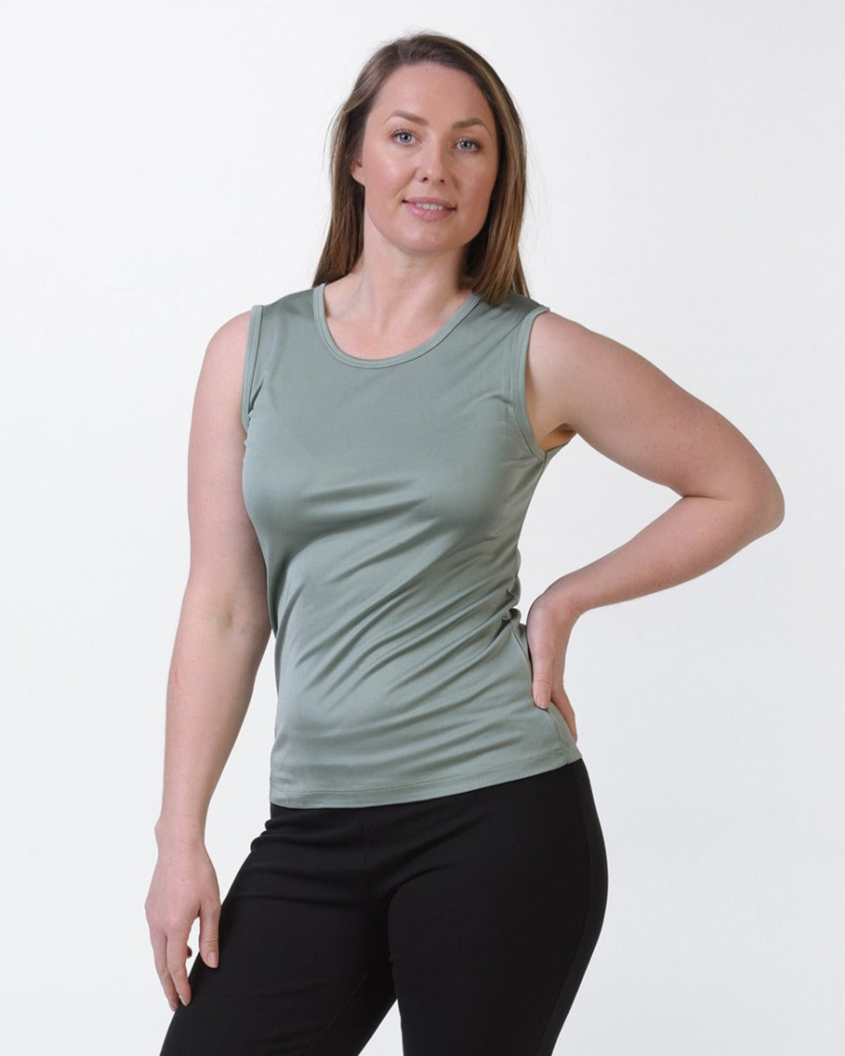 Woman wearing a silk green tank top and black pants on a white background
