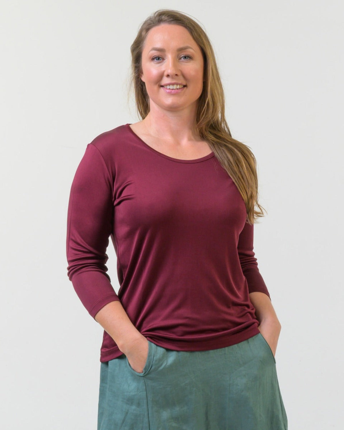 silk Woman wearing a maroon long-sleeve top and green pants against a plain background