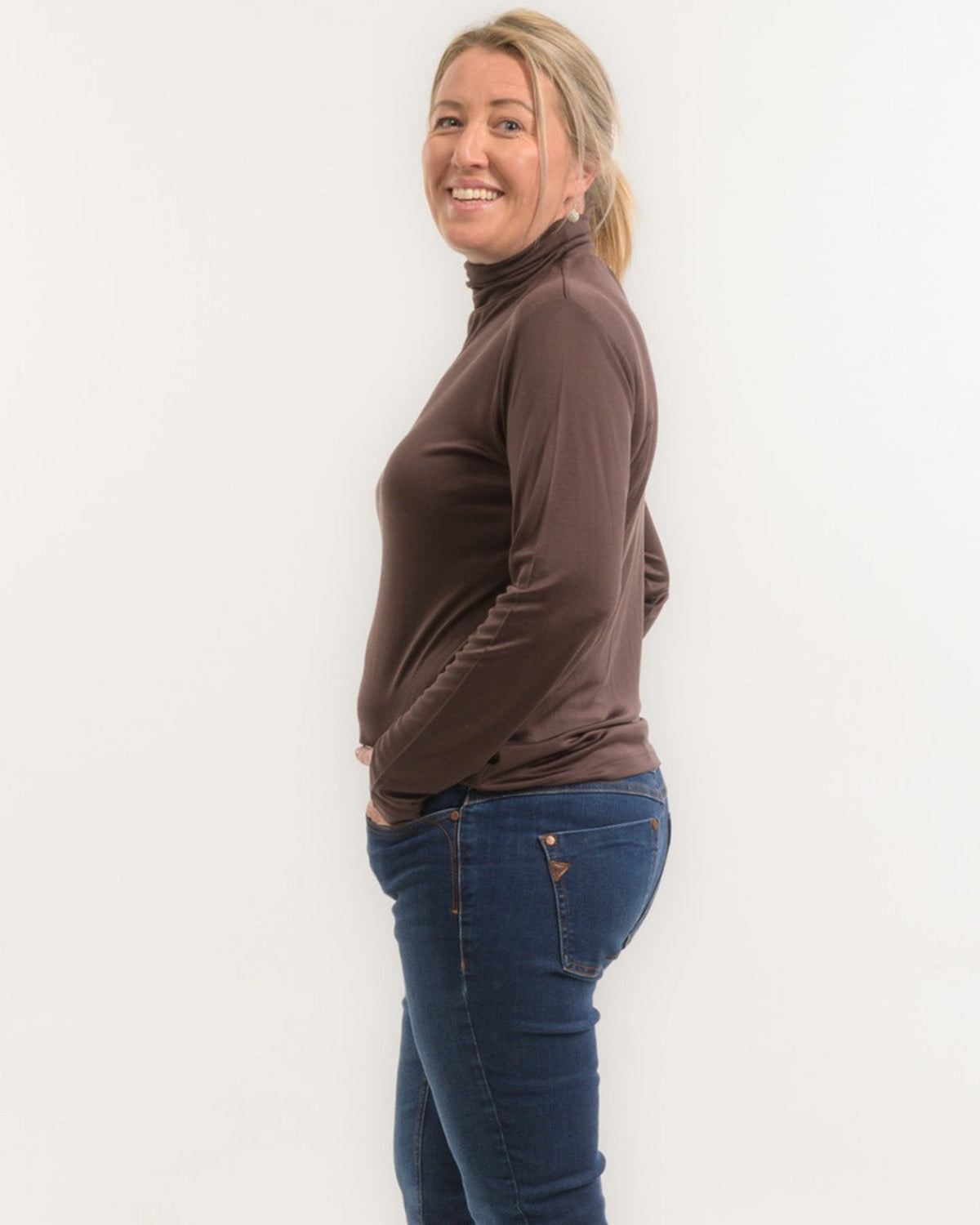 Woman wearing a silk brown turtleneck and blue jeans against a white background