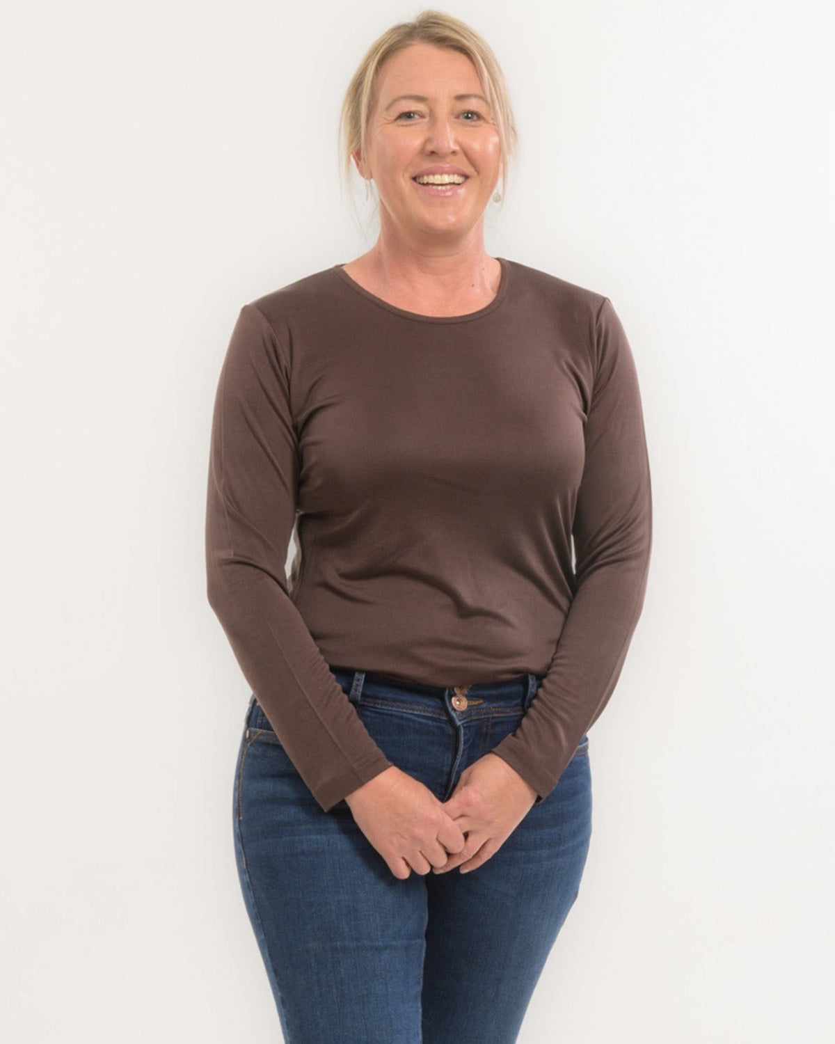 Woman wearing a silk brown long-sleeve shirt and blue jeans against a white background
