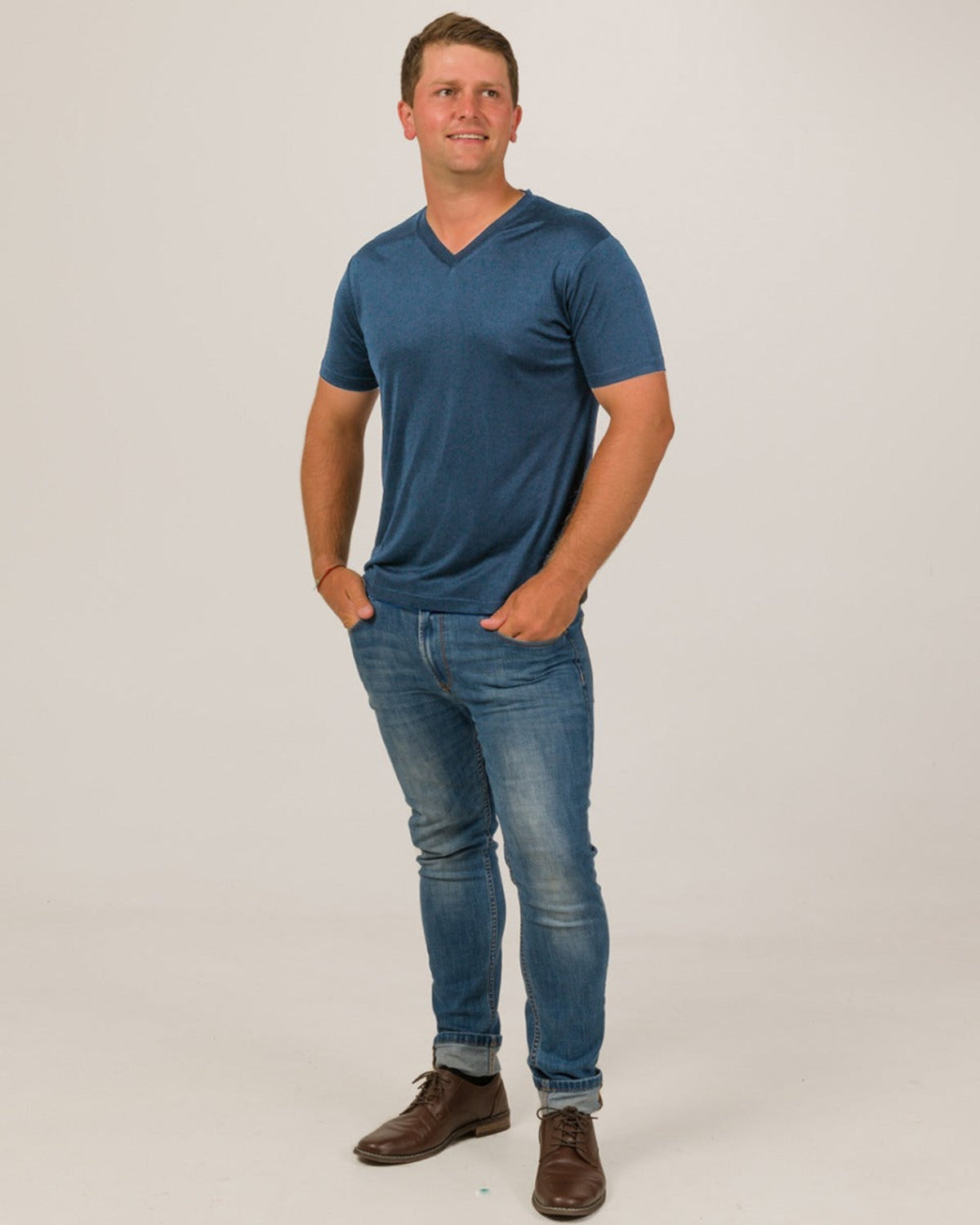 Man wearing a silk blue t-shirt and jeans on a white background
