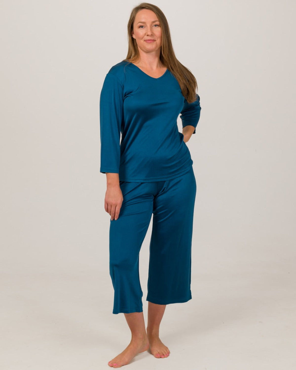 Woman wearing a Peacock blue silk pajama set against a plain background
