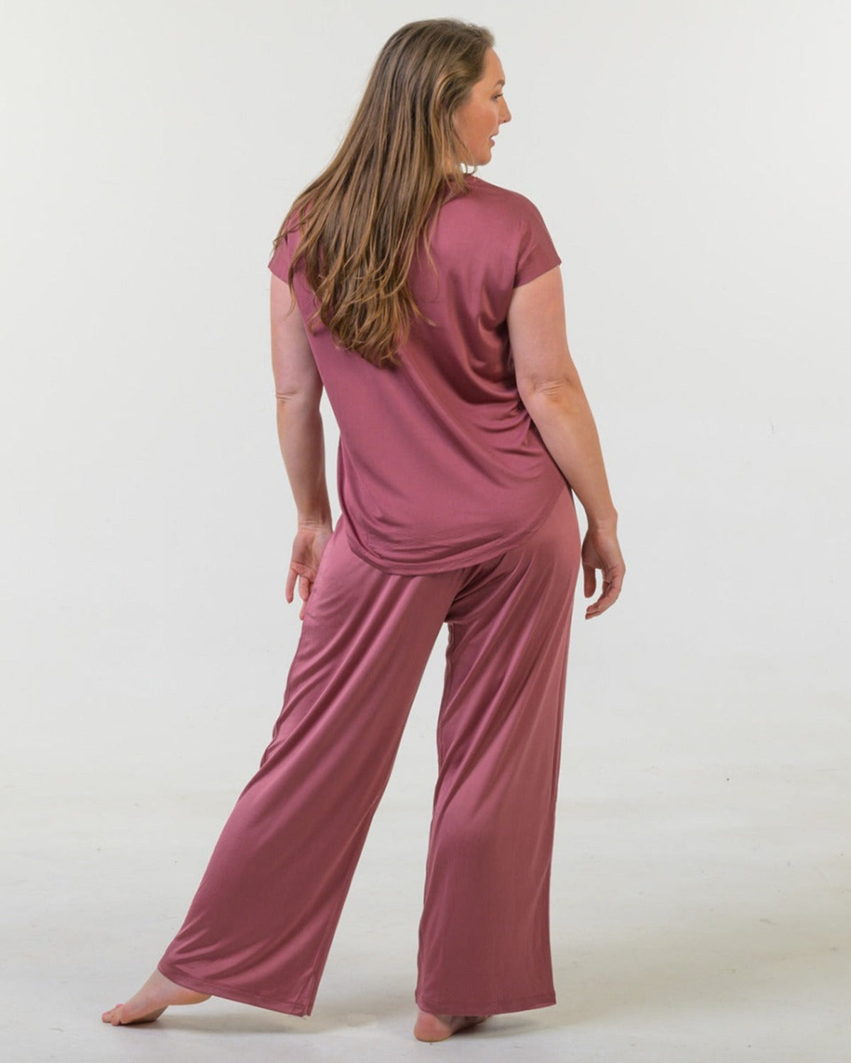 Woman wearing a silk long pants rose pajama set on a white background
