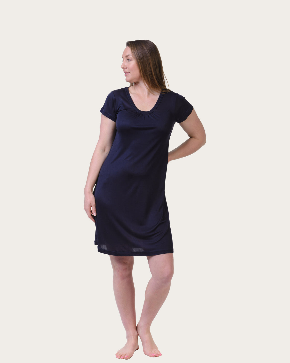 A woman modeling a short-sleeve, knee-length navy blue silk nightgown against a solid, light off-white background.
