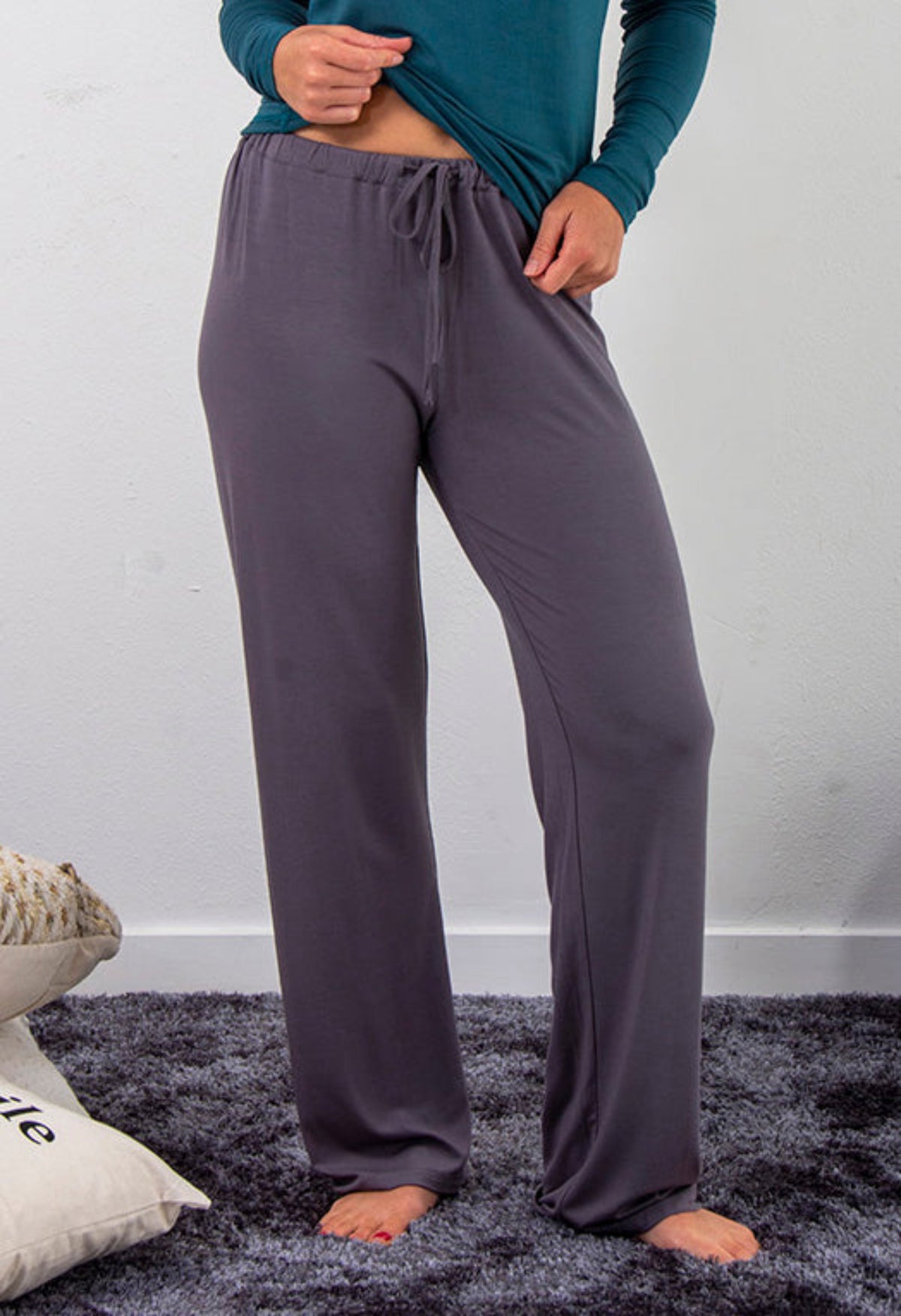 Bamboo leisure  Person wearing gray lounge pants and a teal top on a dark rug with a white wall background.