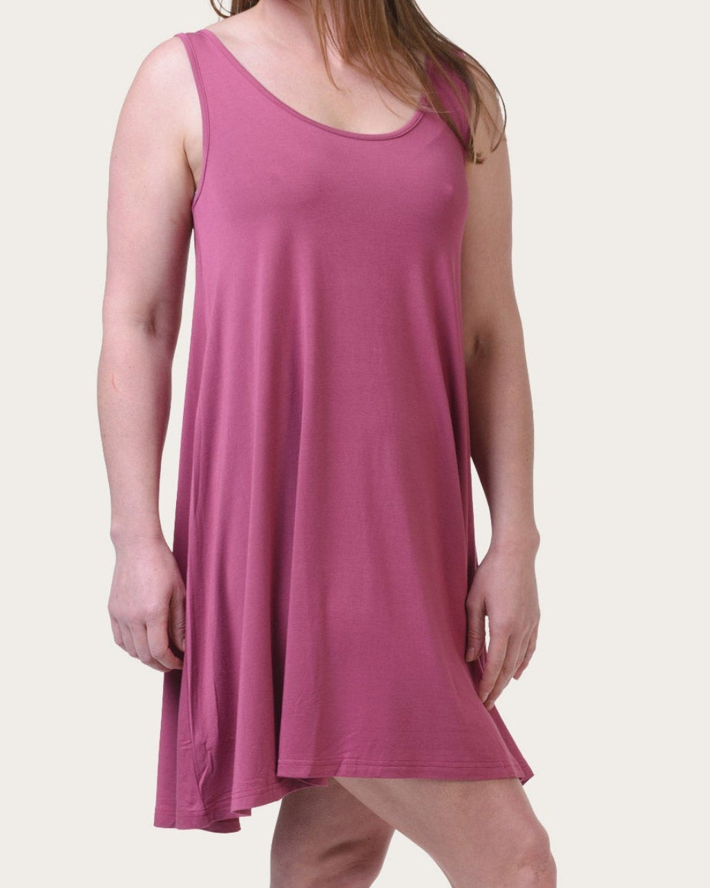 A woman modeling a sleeveless, scoop-neck tunic nightgown in a dusty rose pink color, standing against a solid off-white background.
