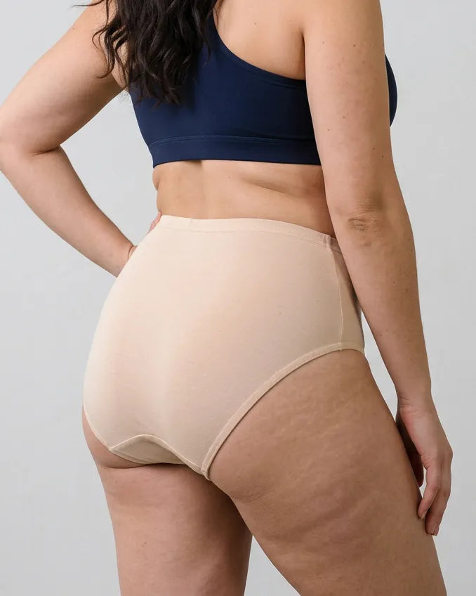A model wearing high-waisted beige shapewear briefs, shown from a rear three-quarter angle against a light gray studio background.