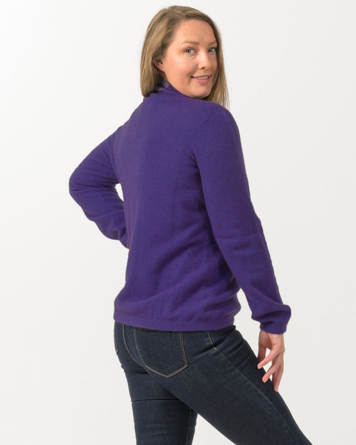 Woman wearing a purple possum merino zip sweater and dark jeans on a white background