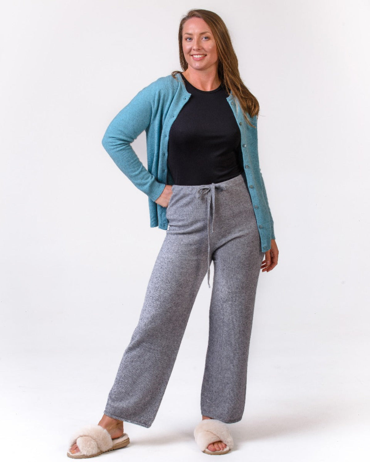 Possum merino Woman wearing a blue cardigan, black top, and gray pants on a white background
