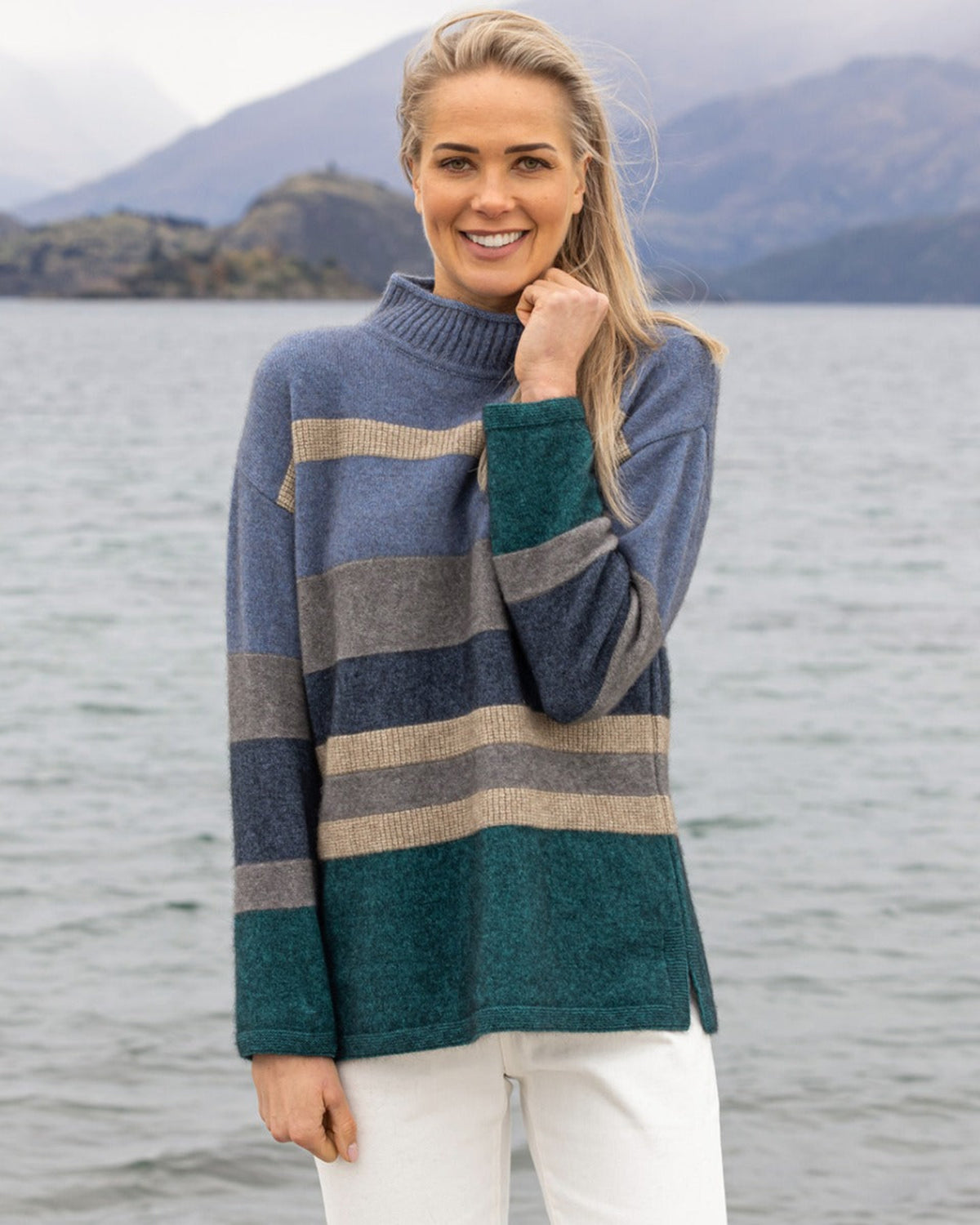 Possum merino Woman wearing a striped sweater by a lake with mountains in the background
