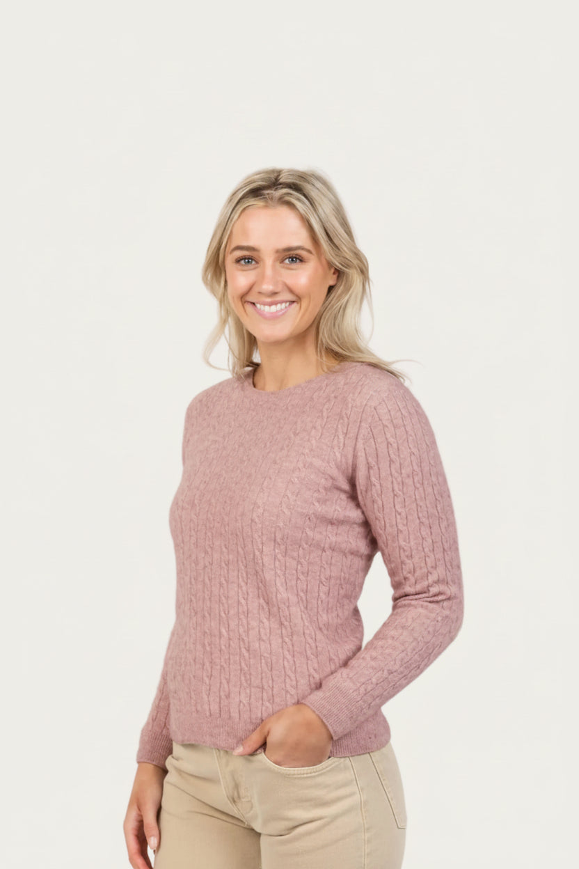 Woman wearing a pink possum merino cable knit sweater on a white background