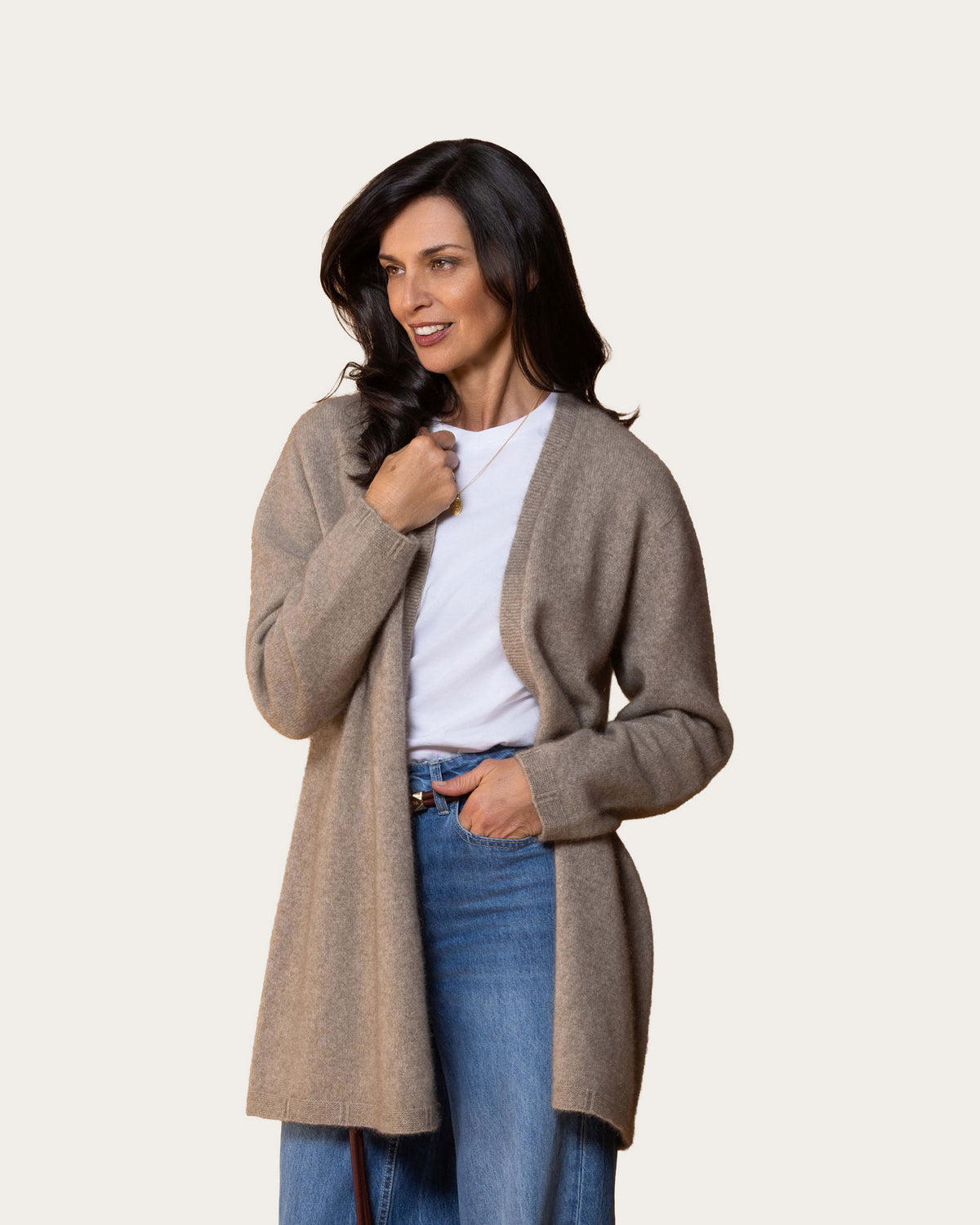 A woman modeling a light brown open-front possum merino cardigan over a white t-shirt and blue jeans, set against a solid off-white background.