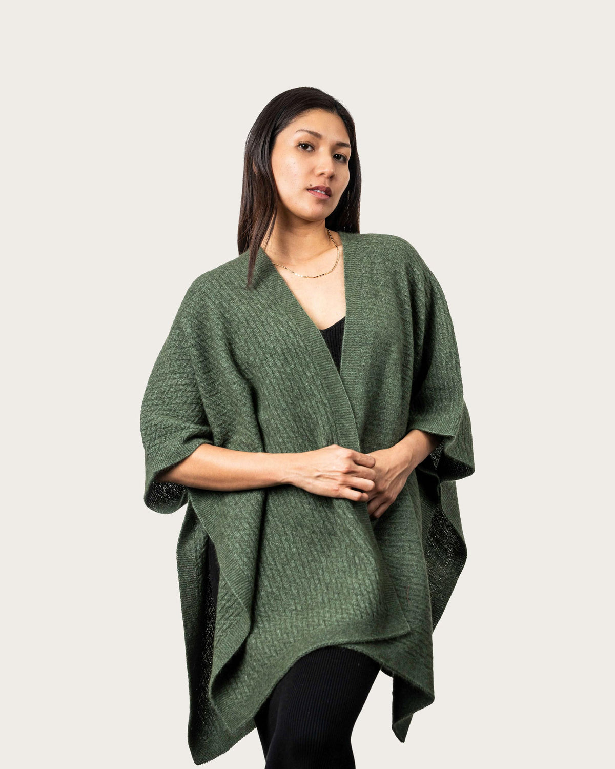 A woman modeling a textured sage green Possum Merino wrap kimono over a black top, photographed against a solid light gray background.