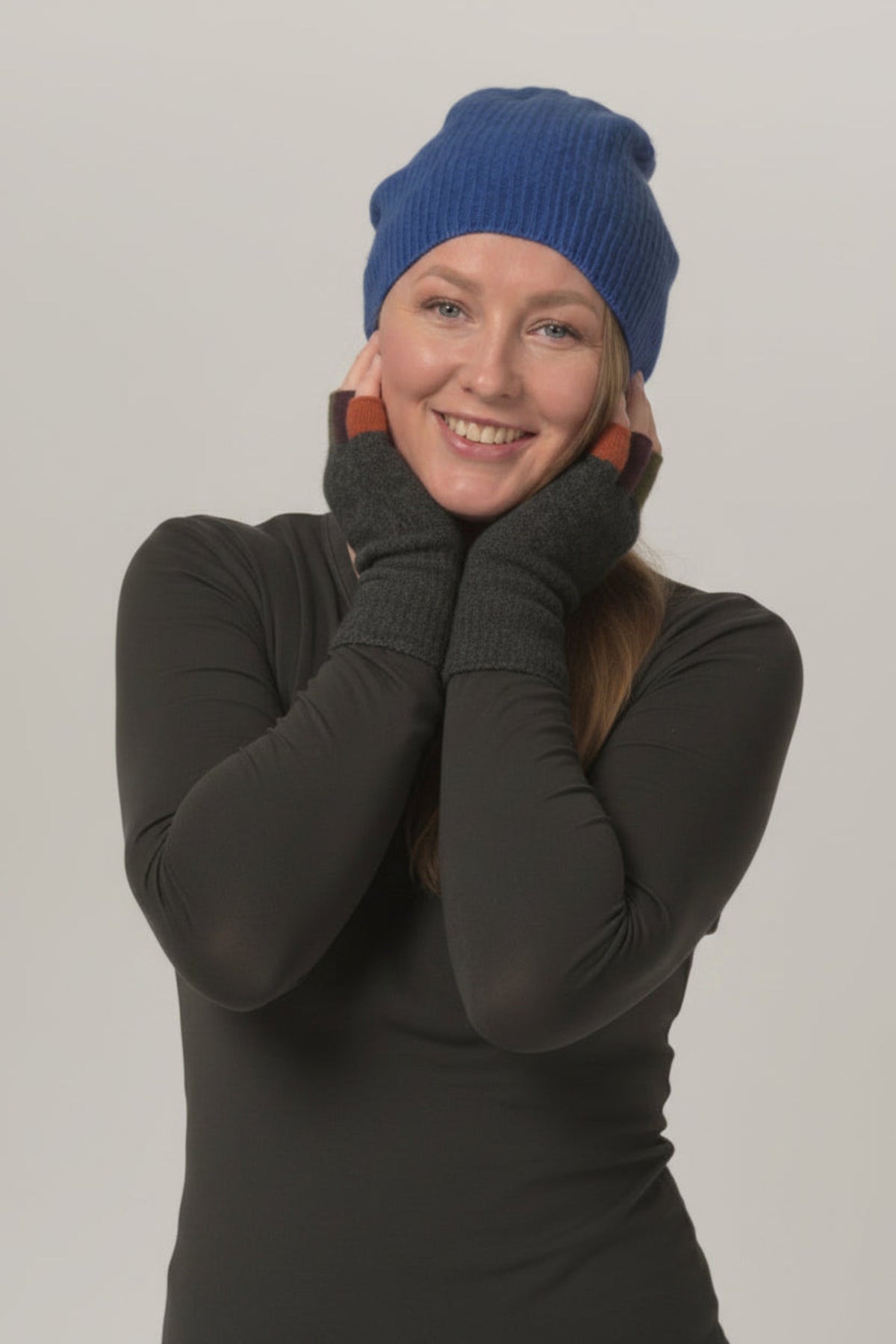 Person wearing a blue beanie and dark gray gloves with multicolor accents on a plain background