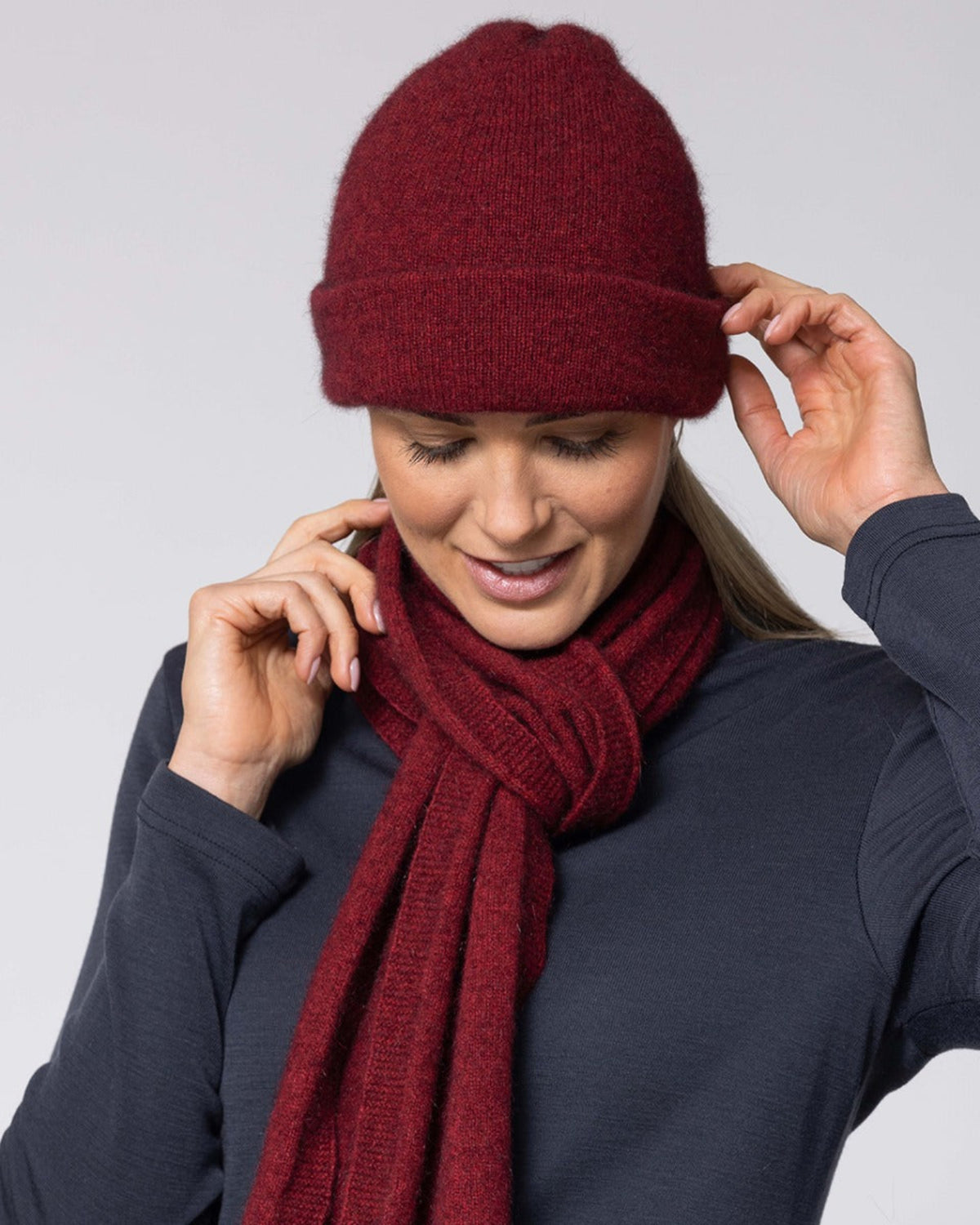 possum merino Woman wearing a red knit hat and scarf against a light gray background