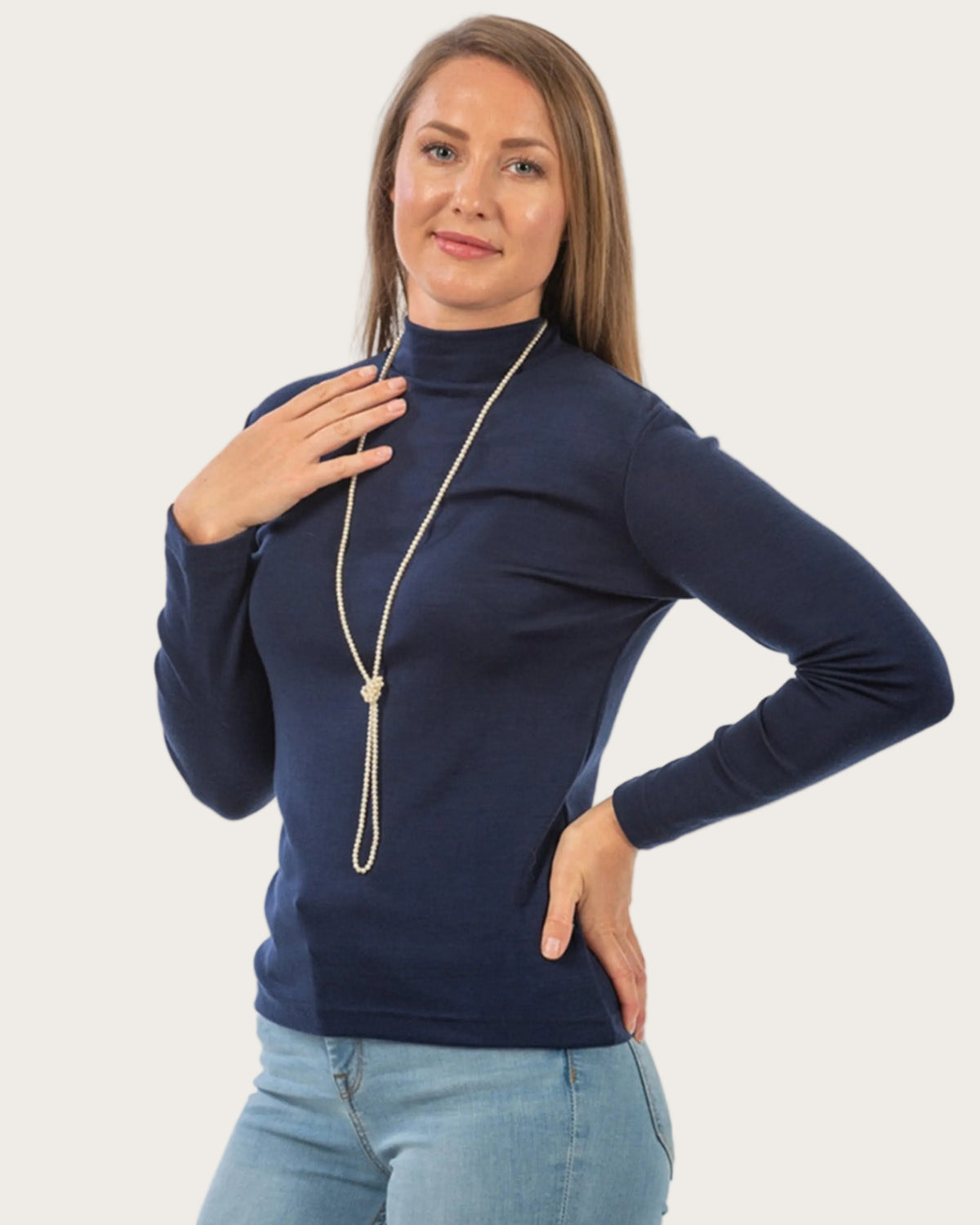 Woman wearing a merino navy blue turtleneck sweater and light blue jeans with a long necklace.