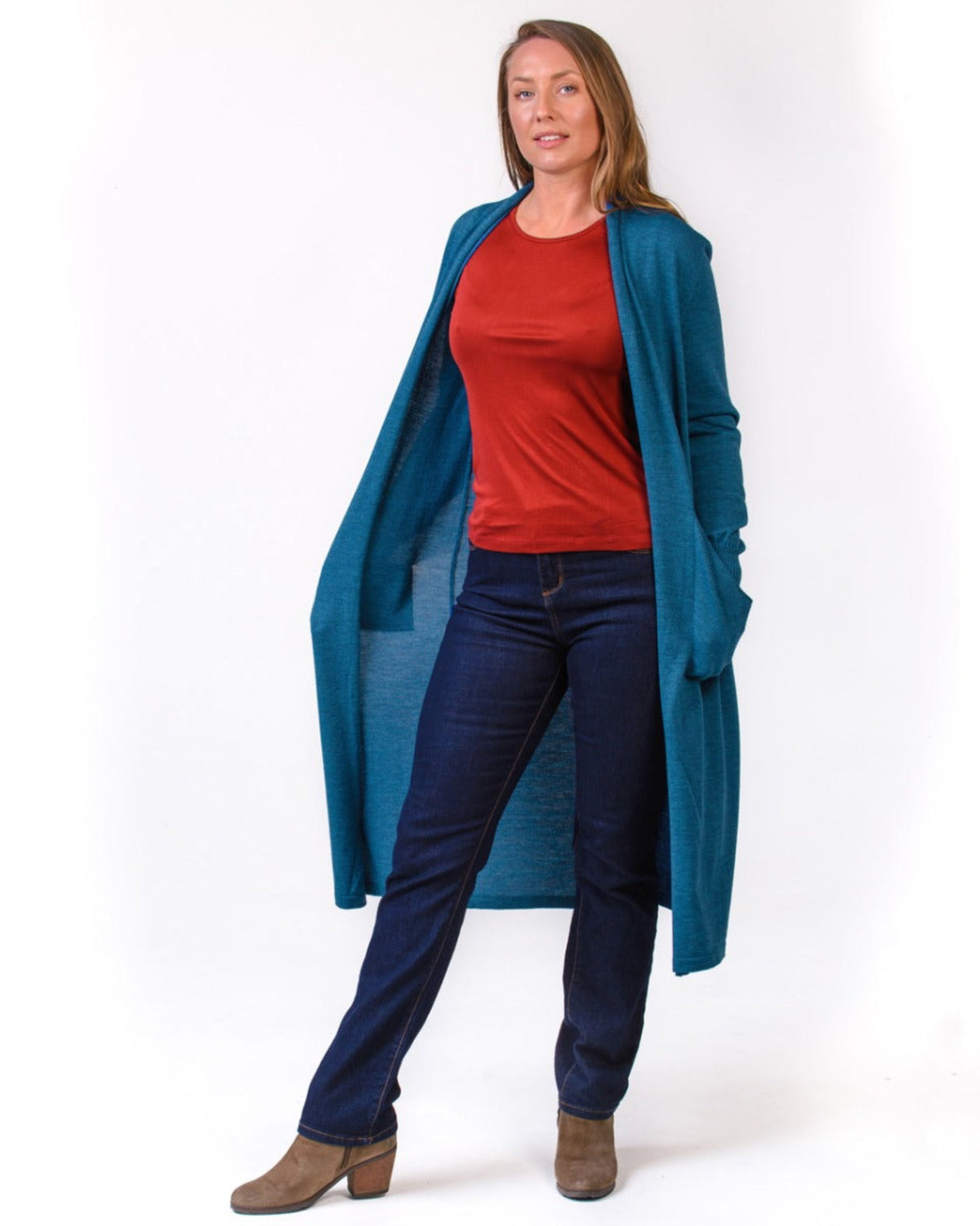Woman wearing a silk long blue cardigan, red shirt, and dark jeans on a white background