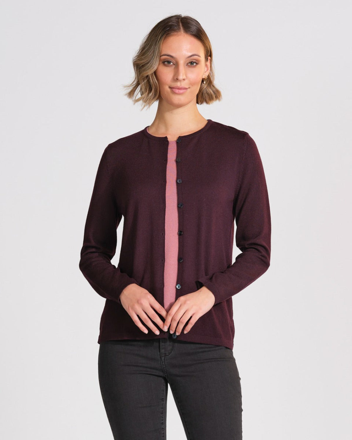 Woman wearing a merino dark purple cardigan with a pink panel on a light gray background