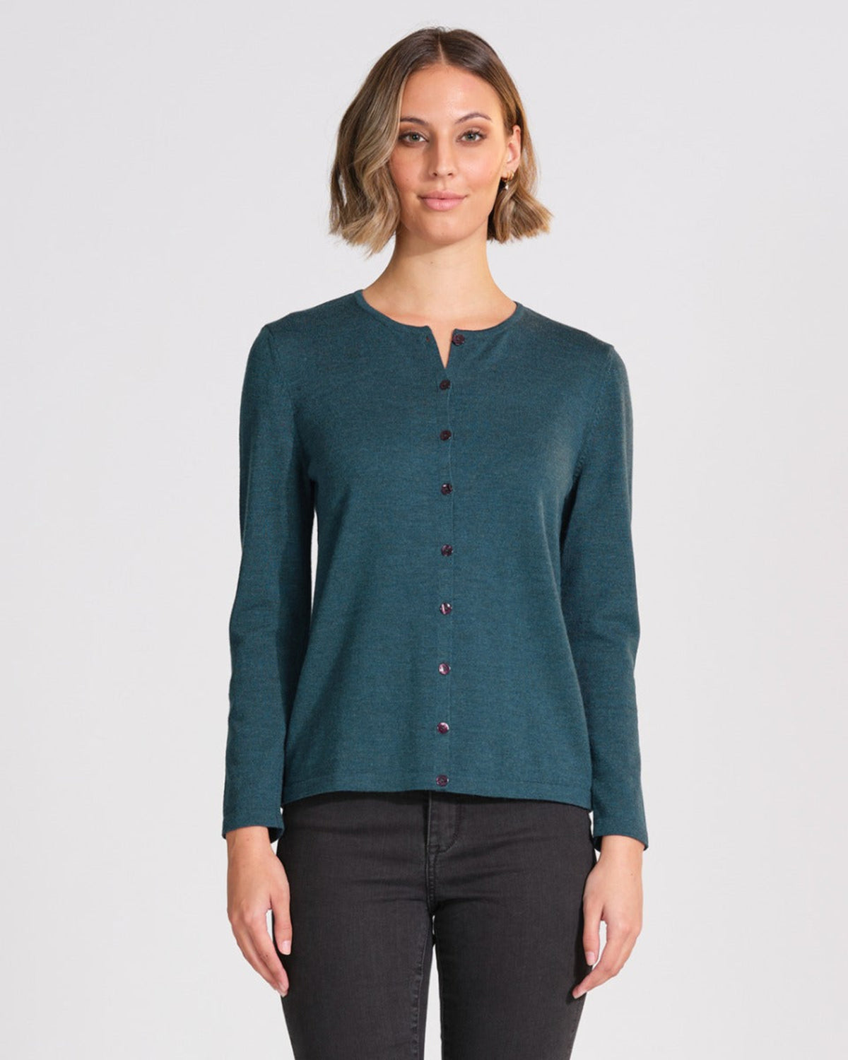 Woman wearing a merino teal long-sleeve shirt with buttons on a white background