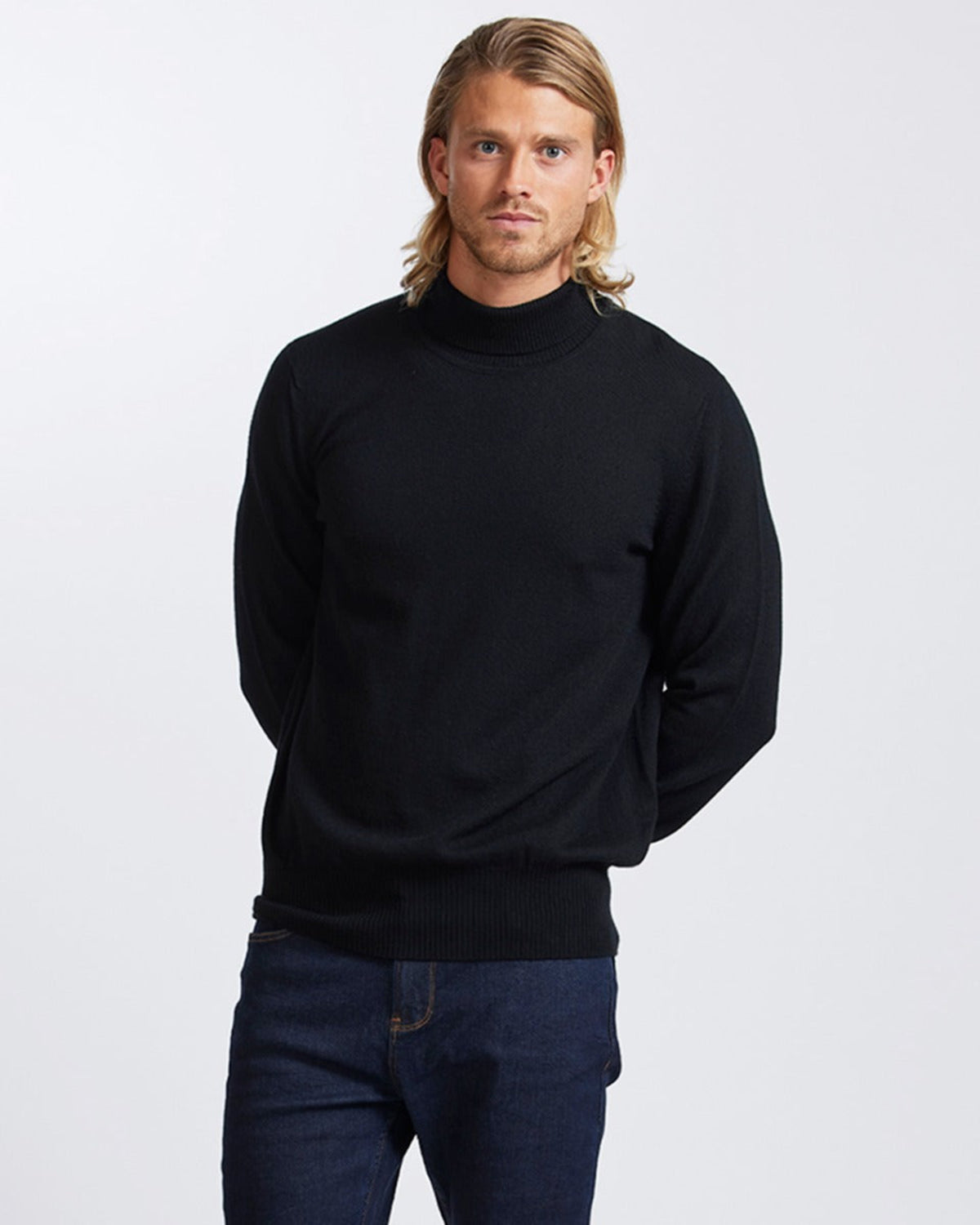 Man wearing a merino black turtleneck sweater and blue jeans on a white background