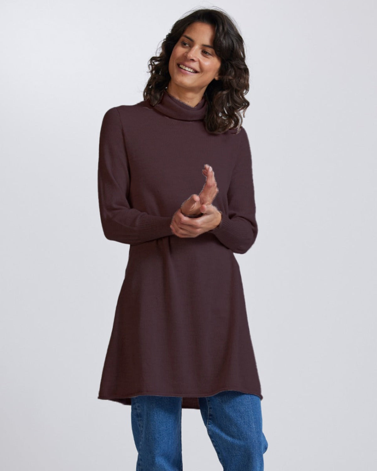 Woman wearing a merino brown turtleneck sweater and blue jeans on a white background