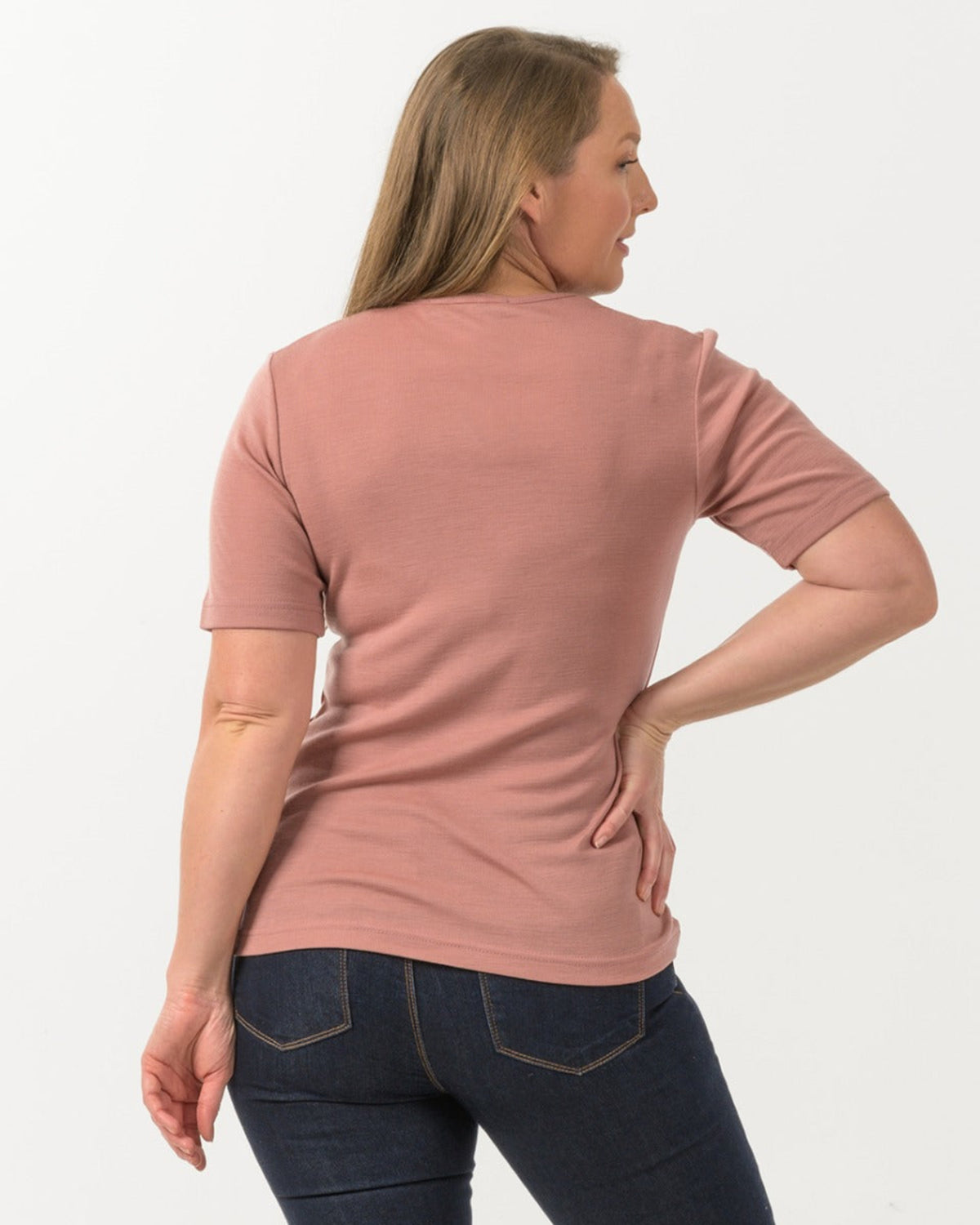 Woman wearing a merino pink t-shirt and dark jeans on a white background