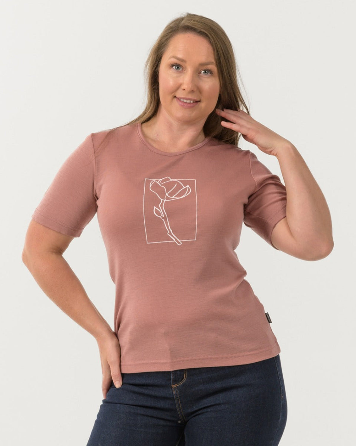Woman wearing a merino pink t-shirt with a white graphic on a white background