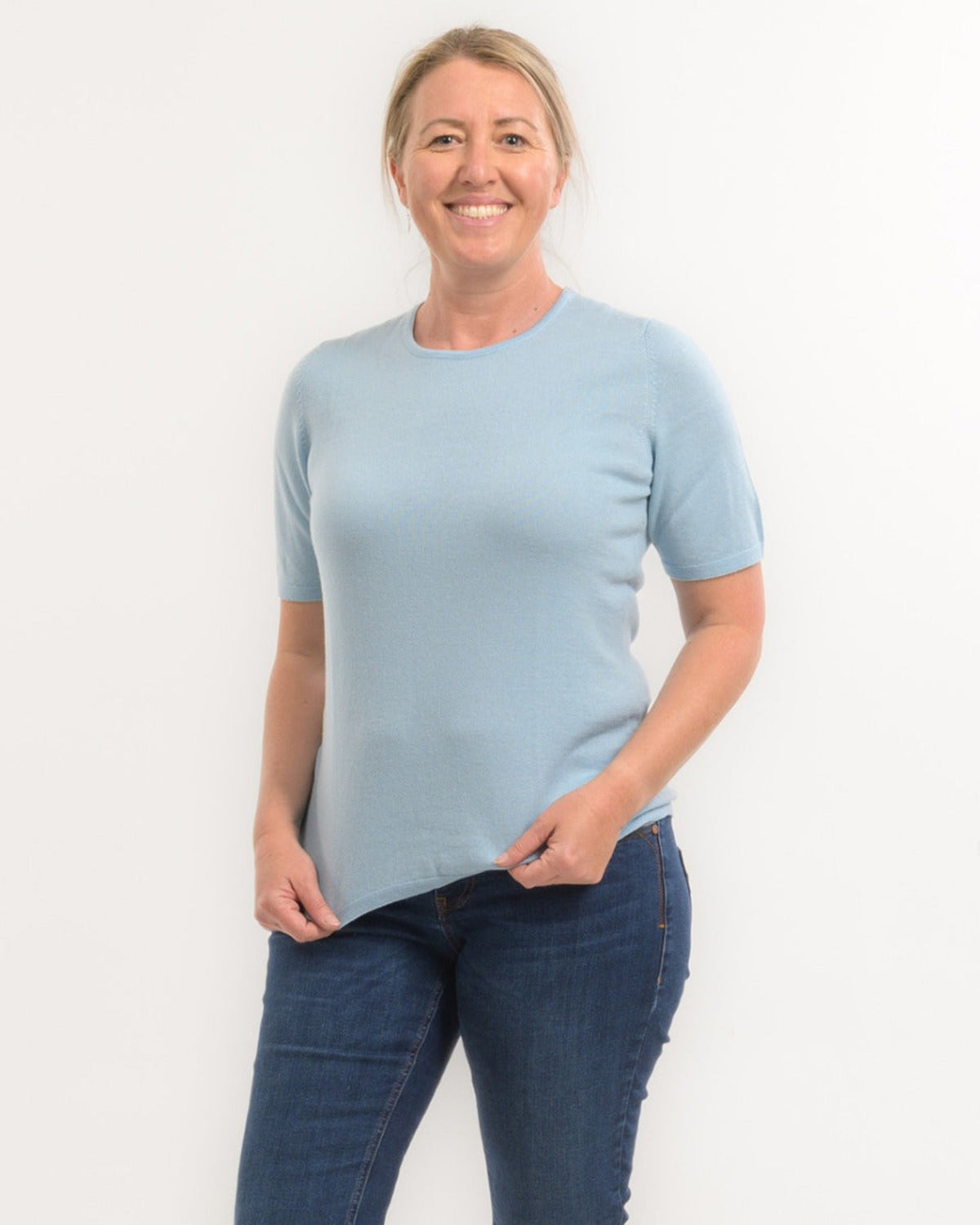 Woman wearing a merino light blue t-shirt and dark blue jeans against a white background