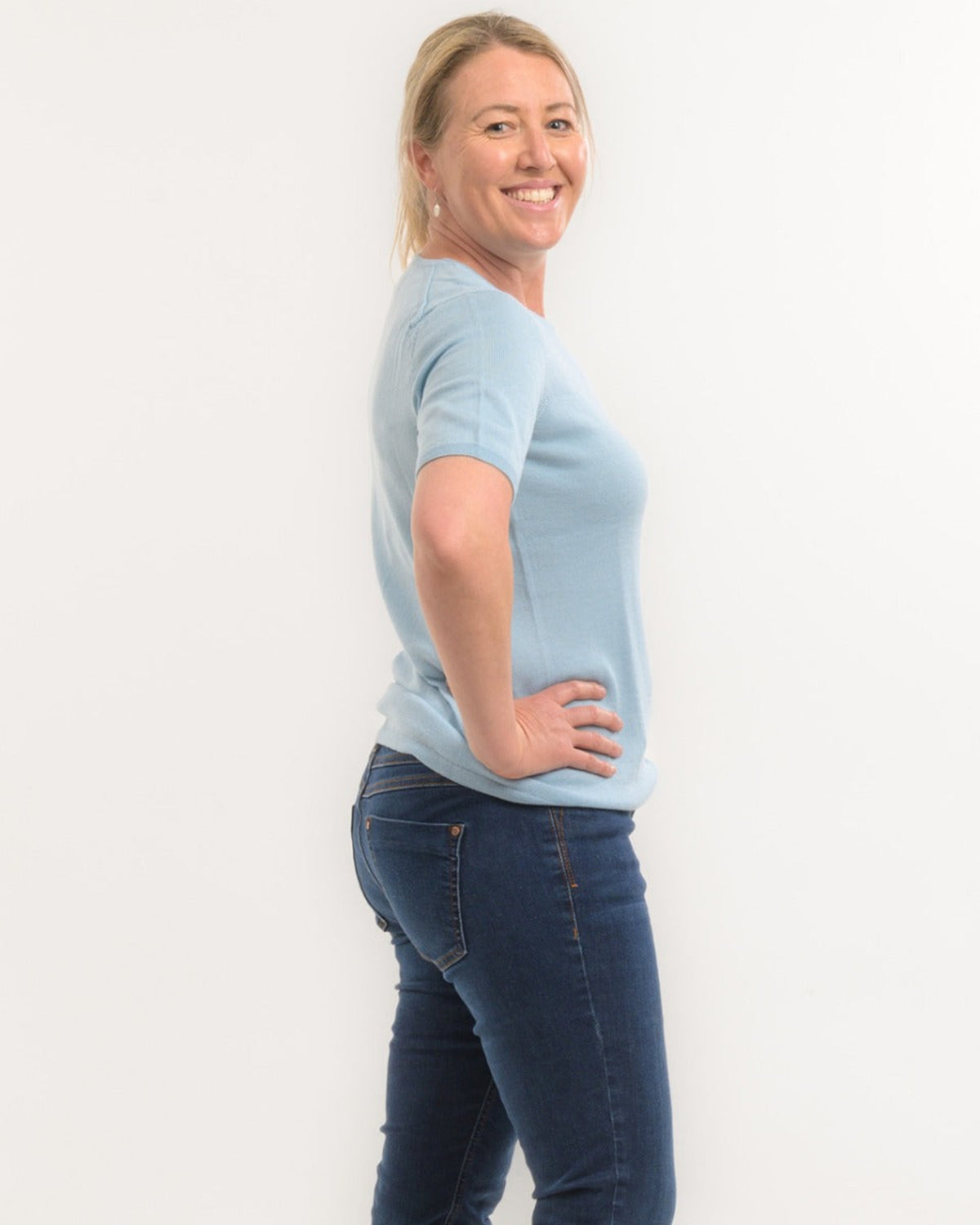 Woman wearing a merino light blue sweater and dark blue jeans against a white background