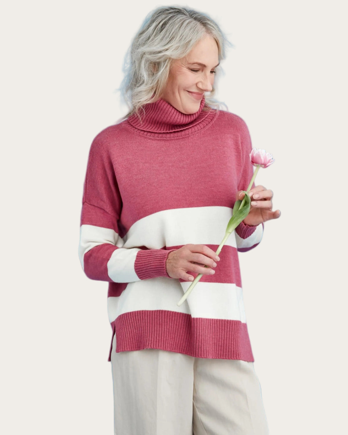 Woman wearing a merino pink and white striped sweater holding a flower against a blue background