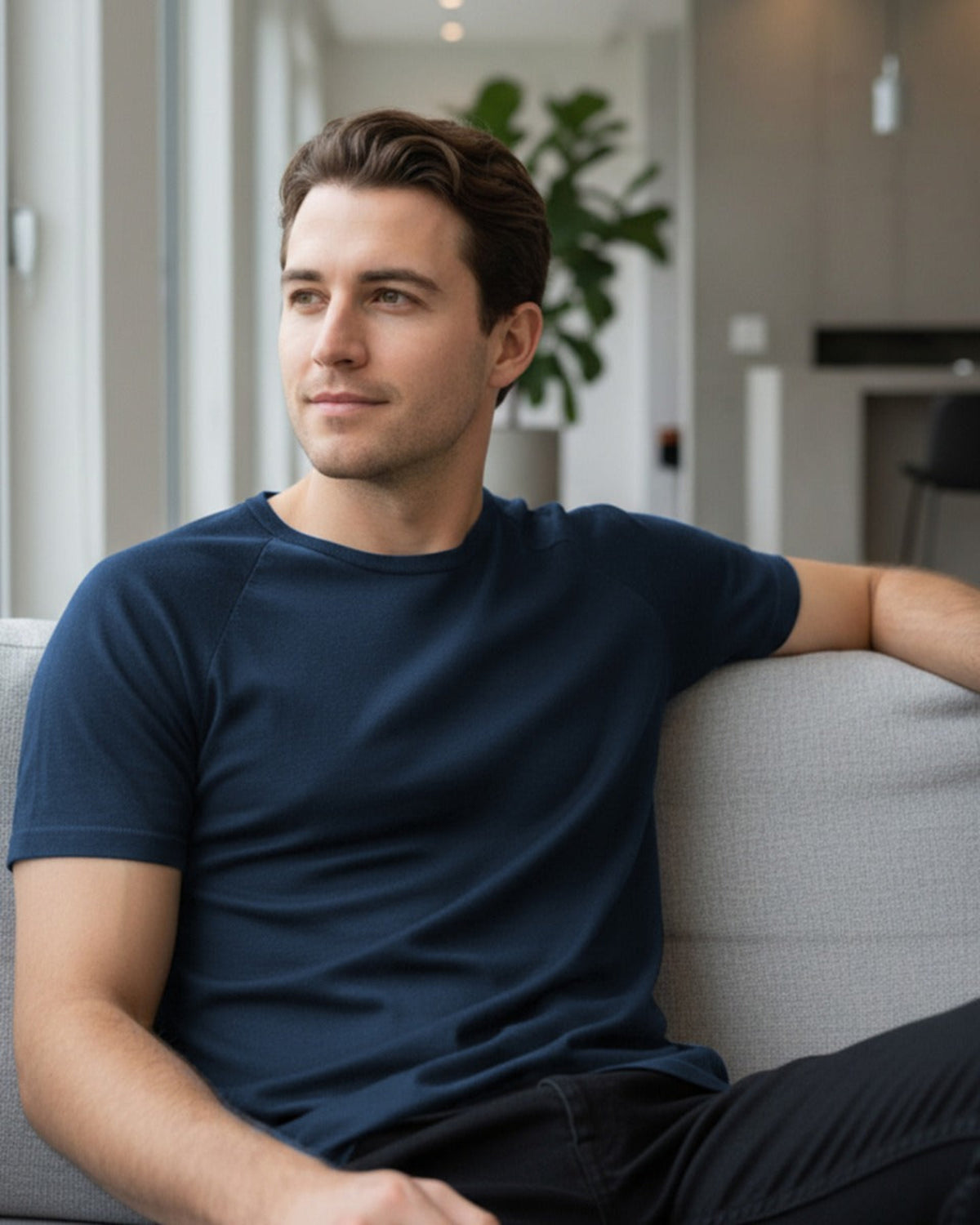 Man sitting on a couch wearing a merino  blue t-shirt in a modern living room.