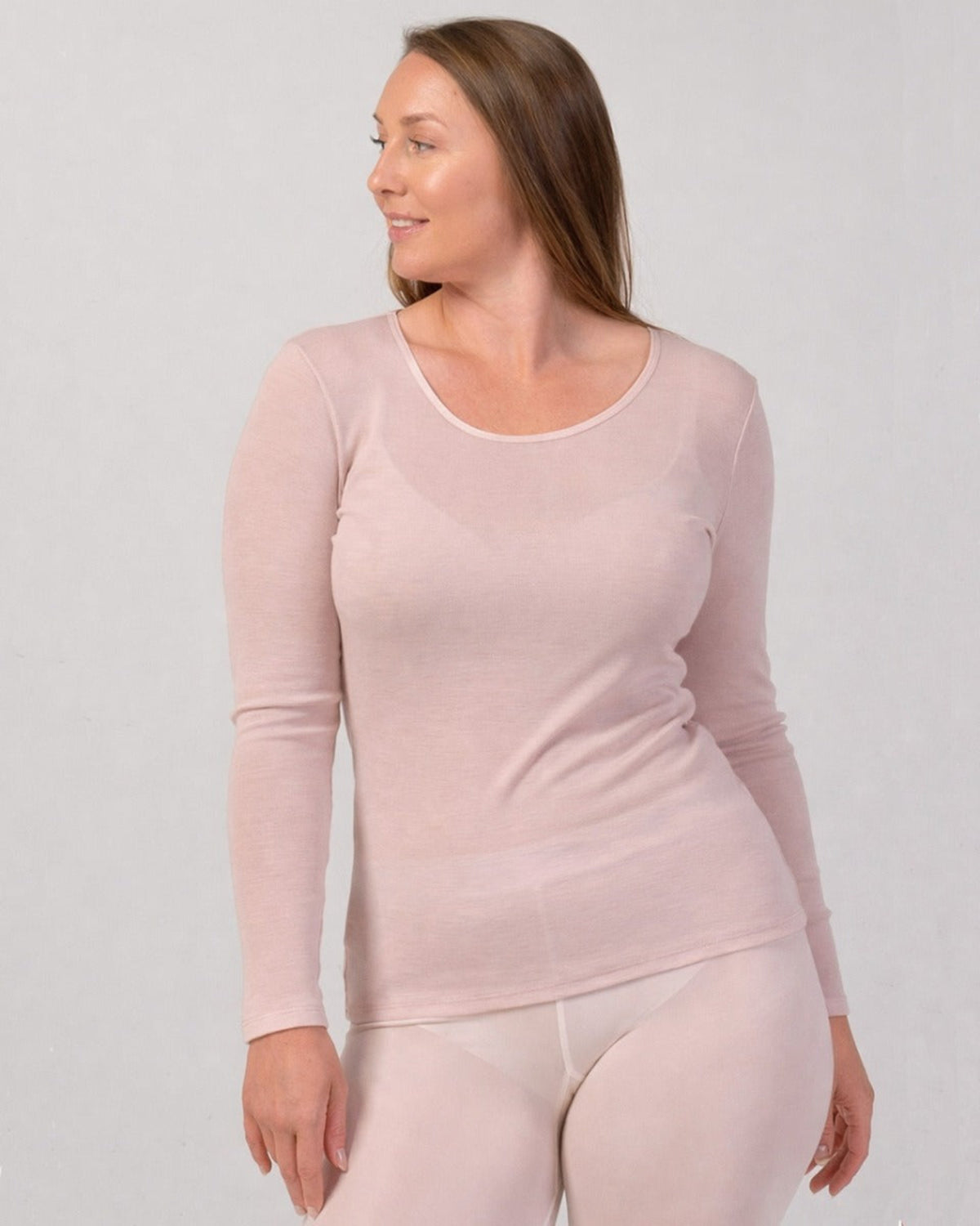 Woman wearing a merino  pink long-sleeve top and pants against a light gray background