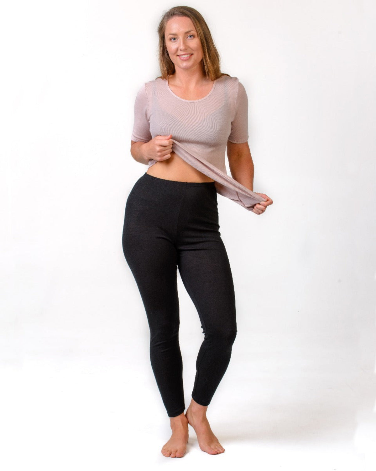 Woman wearing a merino beige crop top and black leggings on a white background