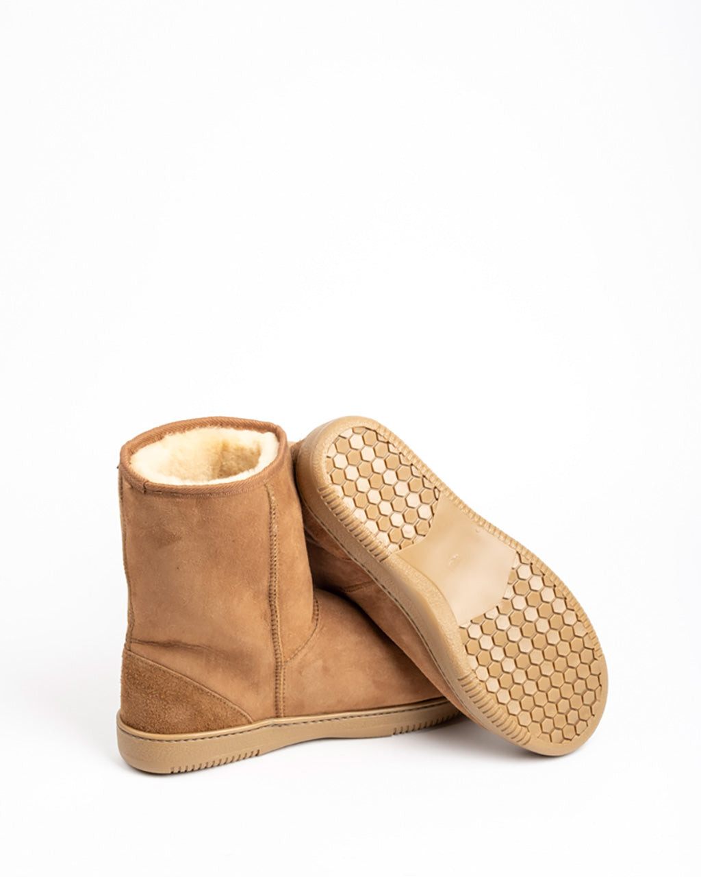 A pair of tan suede ankle boots with a soft cream shearling lining, shown from the side and bottom to display the sole tread pattern, on a white background.