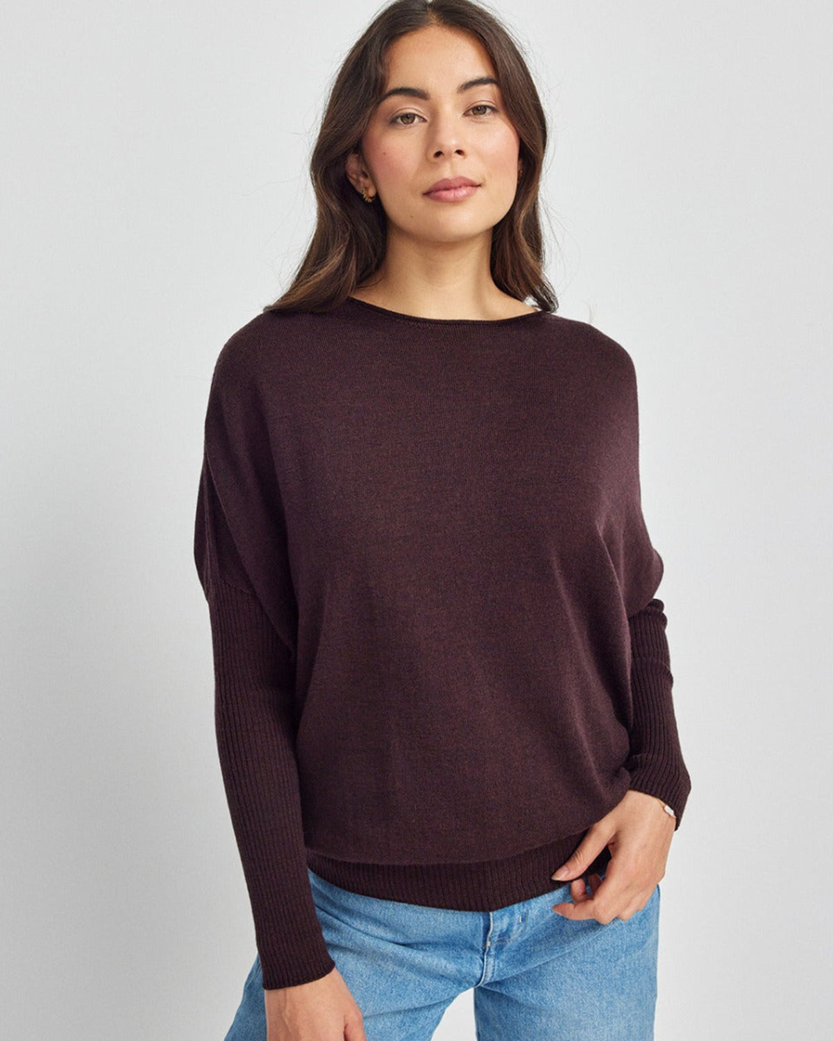 Woman wearing a dark brown merino sweater and light blue jeans on a white background