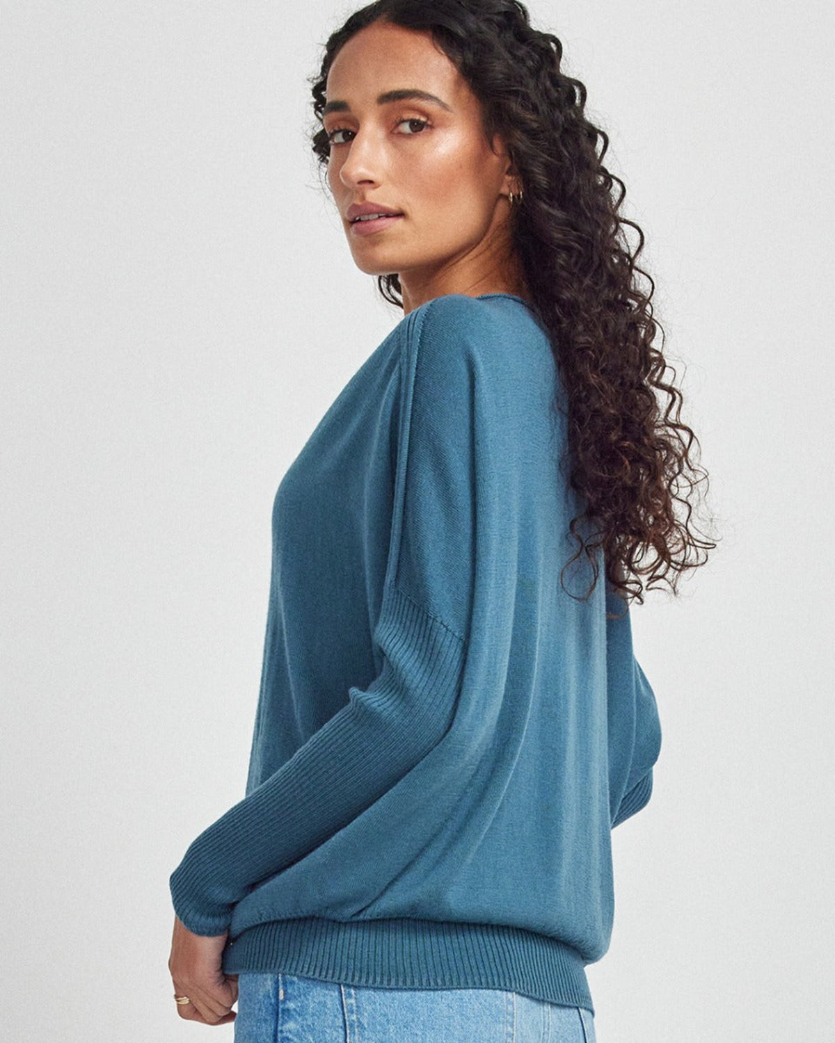 Woman wearing a merino teal sweater against a white background