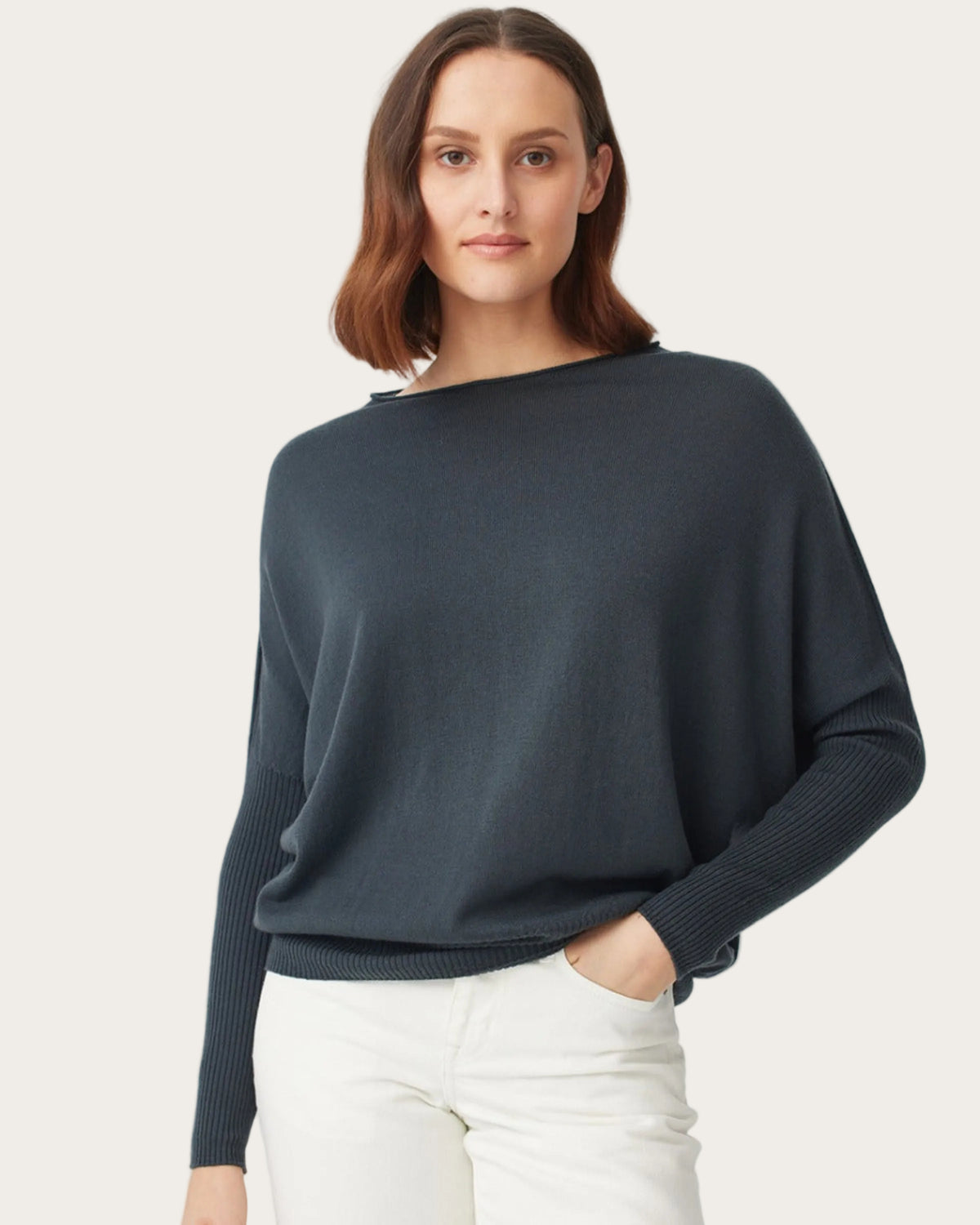 Woman wearing merino a dark blue sweater and white pants on a light gray background