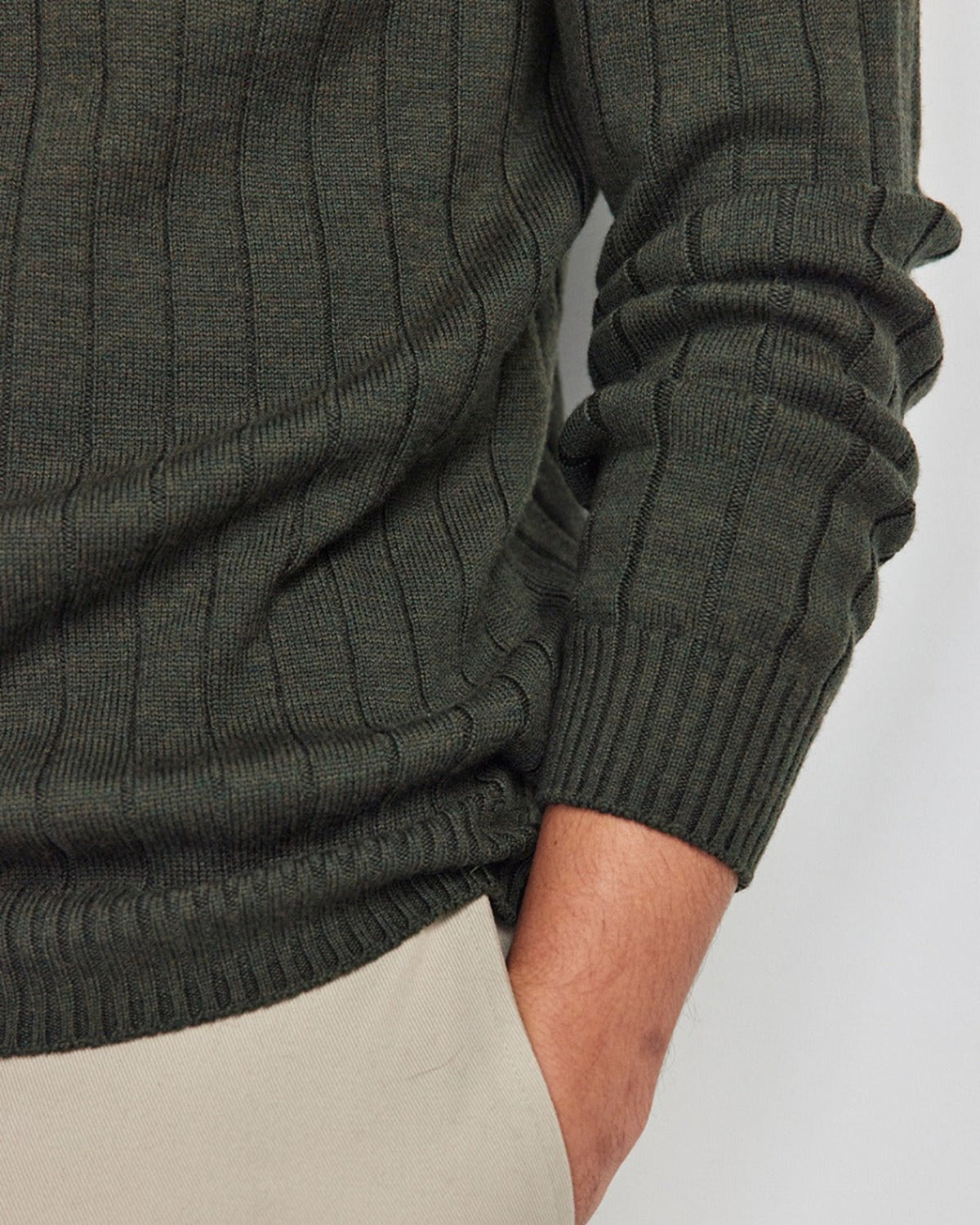 Close-up of a person wearing a merino dark green ribbed sweater on a light background