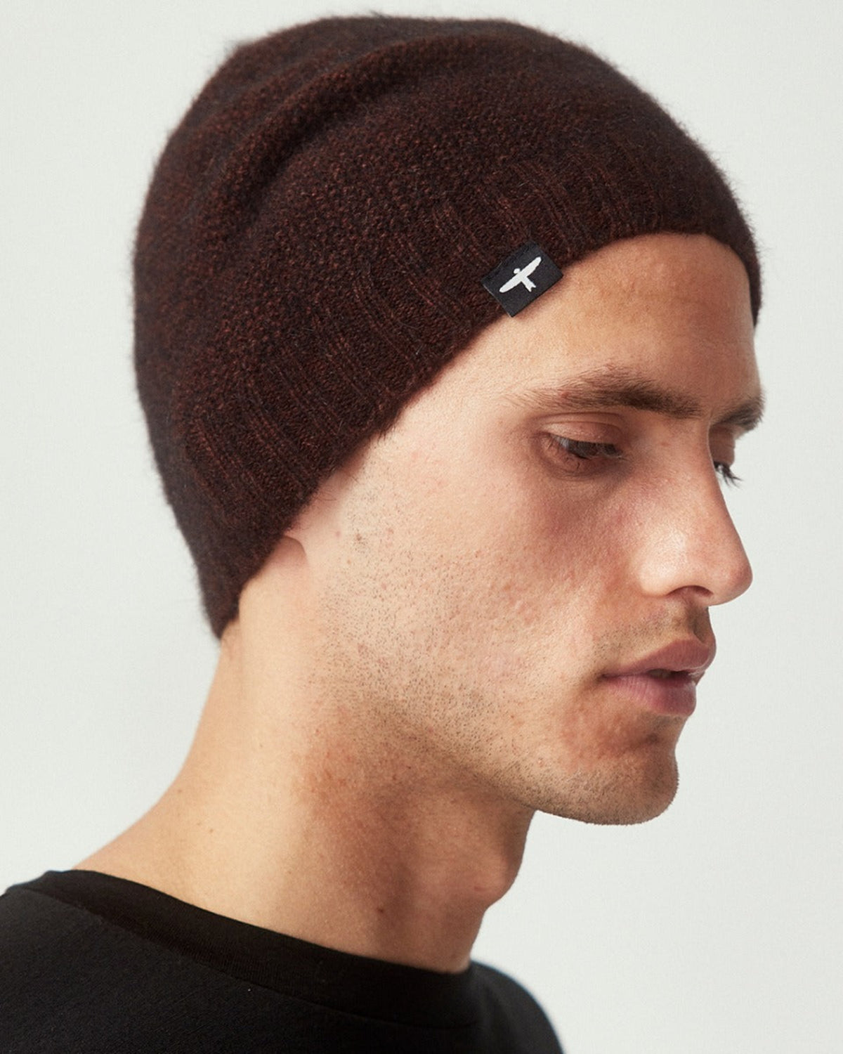 possum merino Man wearing a brown beanie with a logo on a light gray background