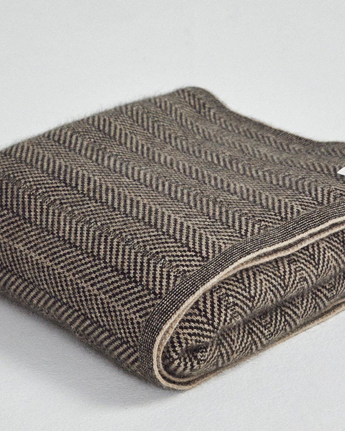 A folded herringbone pattern wool blanket in brown and beige tones, shown on a light gray background.