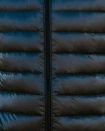 Man wearing a black puffer vest standing on a wooden dock by a lake.