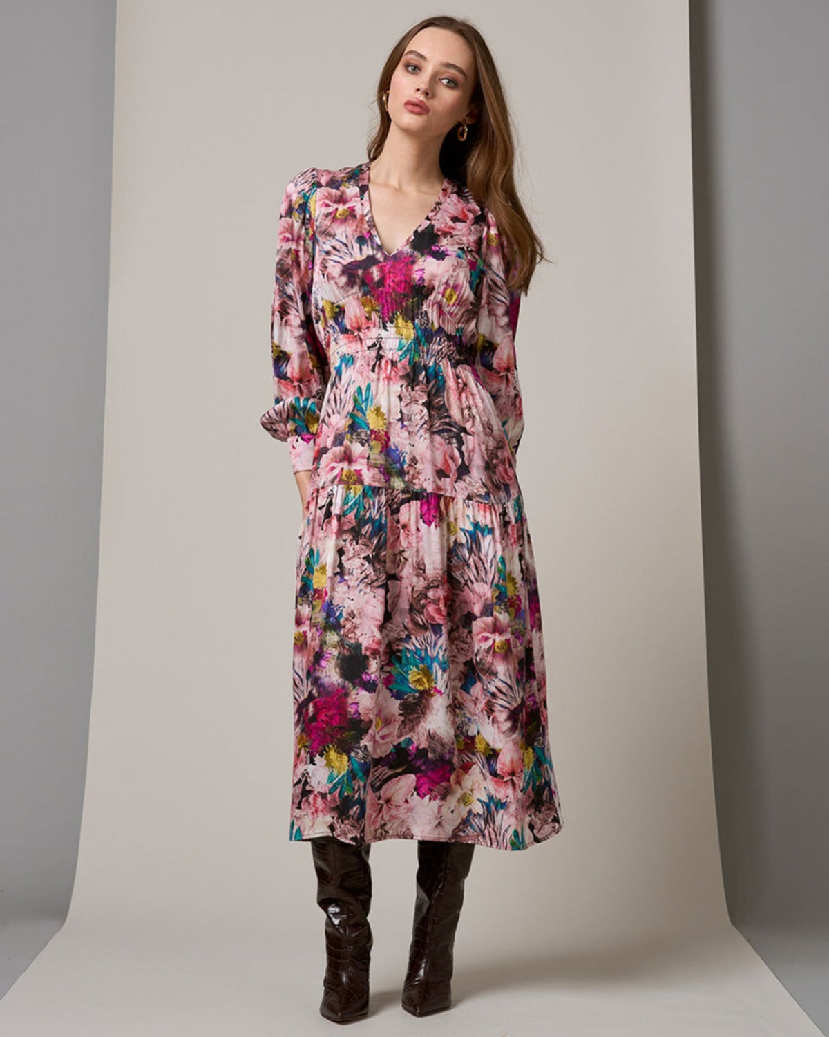 Woman wearing a colorful floral dress with brown boots on a neutral background