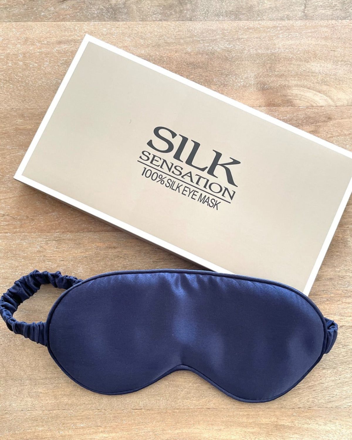 Blue silk eye mask with 'Silk Sensation' packaging on a wooden surface