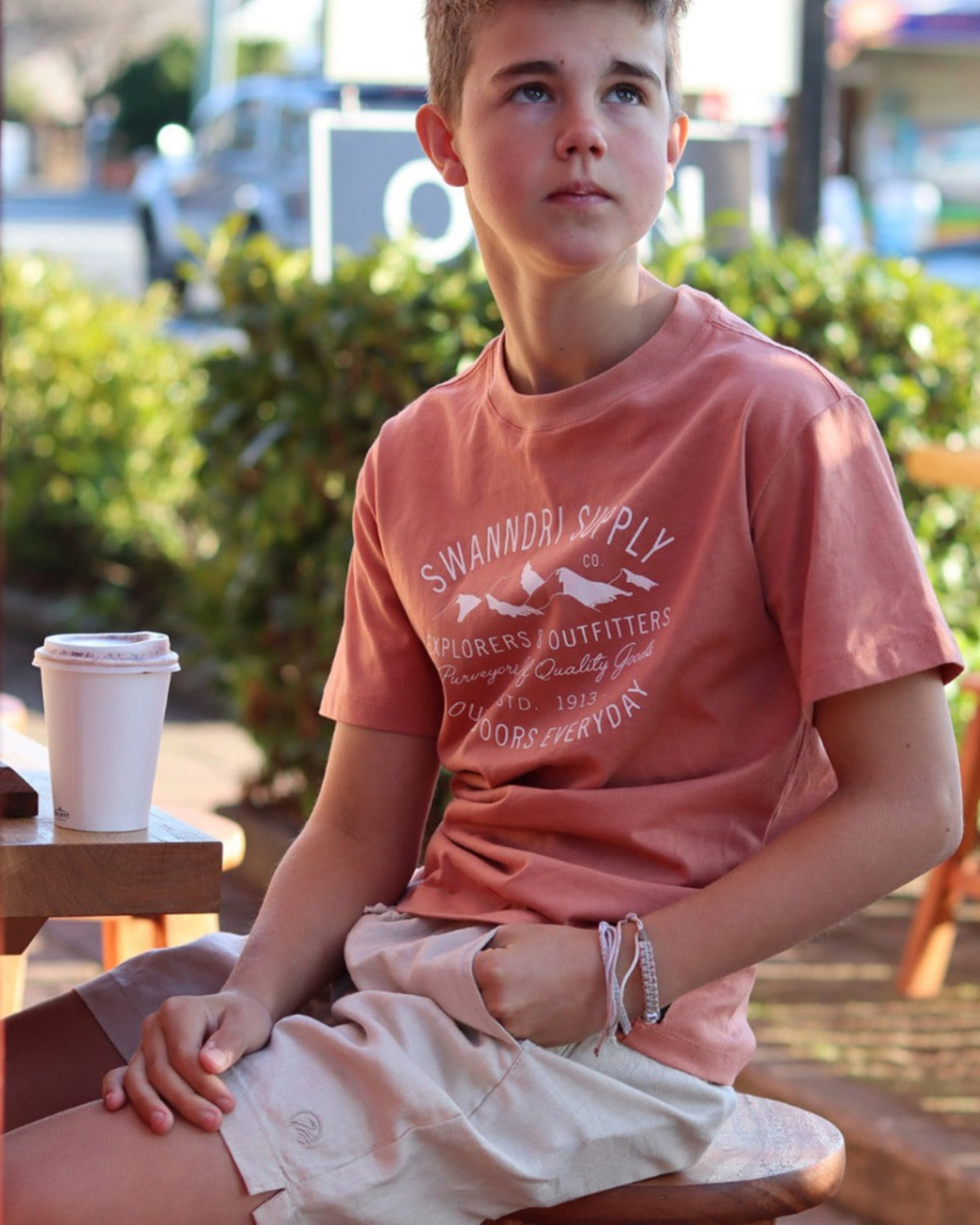 Cotton Young boy wearing a pink t-shirt with text, sitting outdoors.