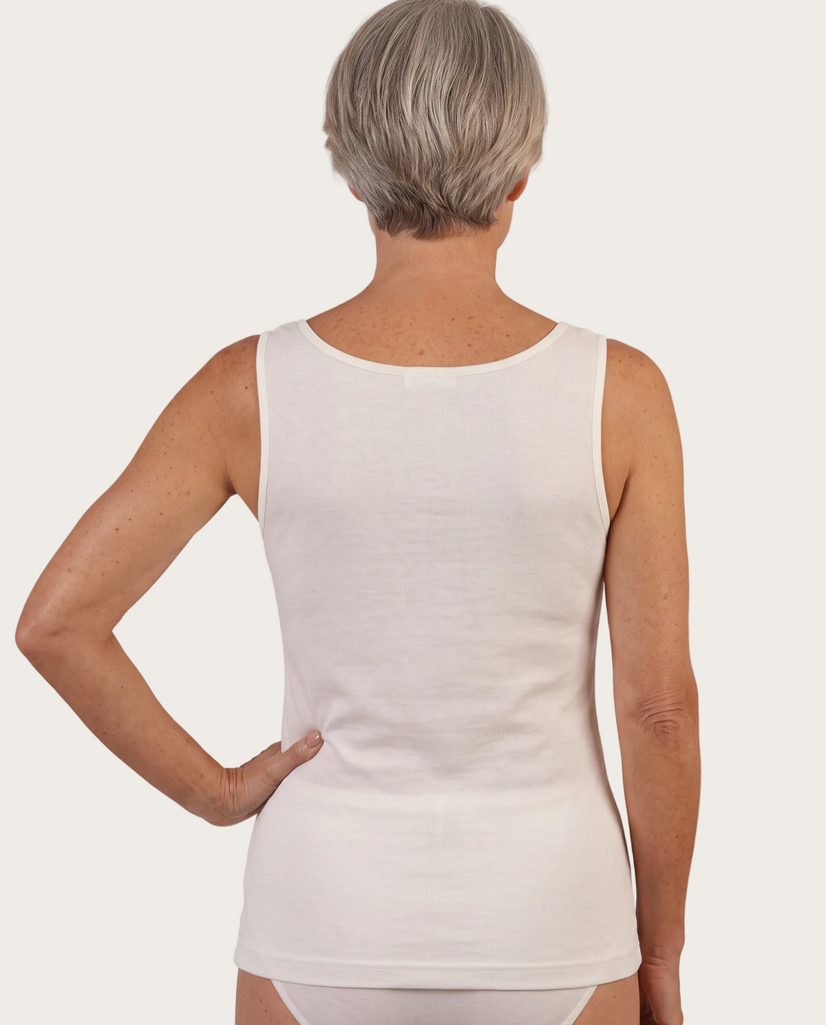 A woman shown from the back wearing a plain sleeveless white tank top against a clean white studio background.