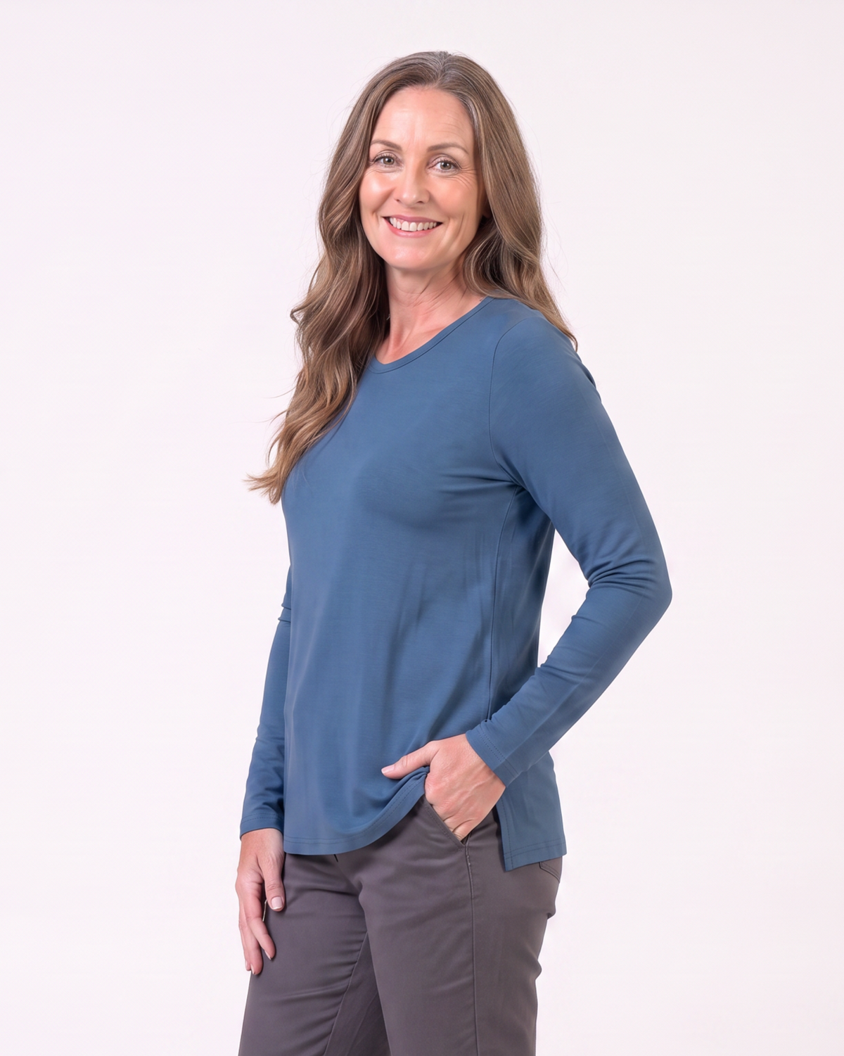 A woman modeling a slate blue long-sleeve V-neck top and dark gray pants against a plain white studio background.