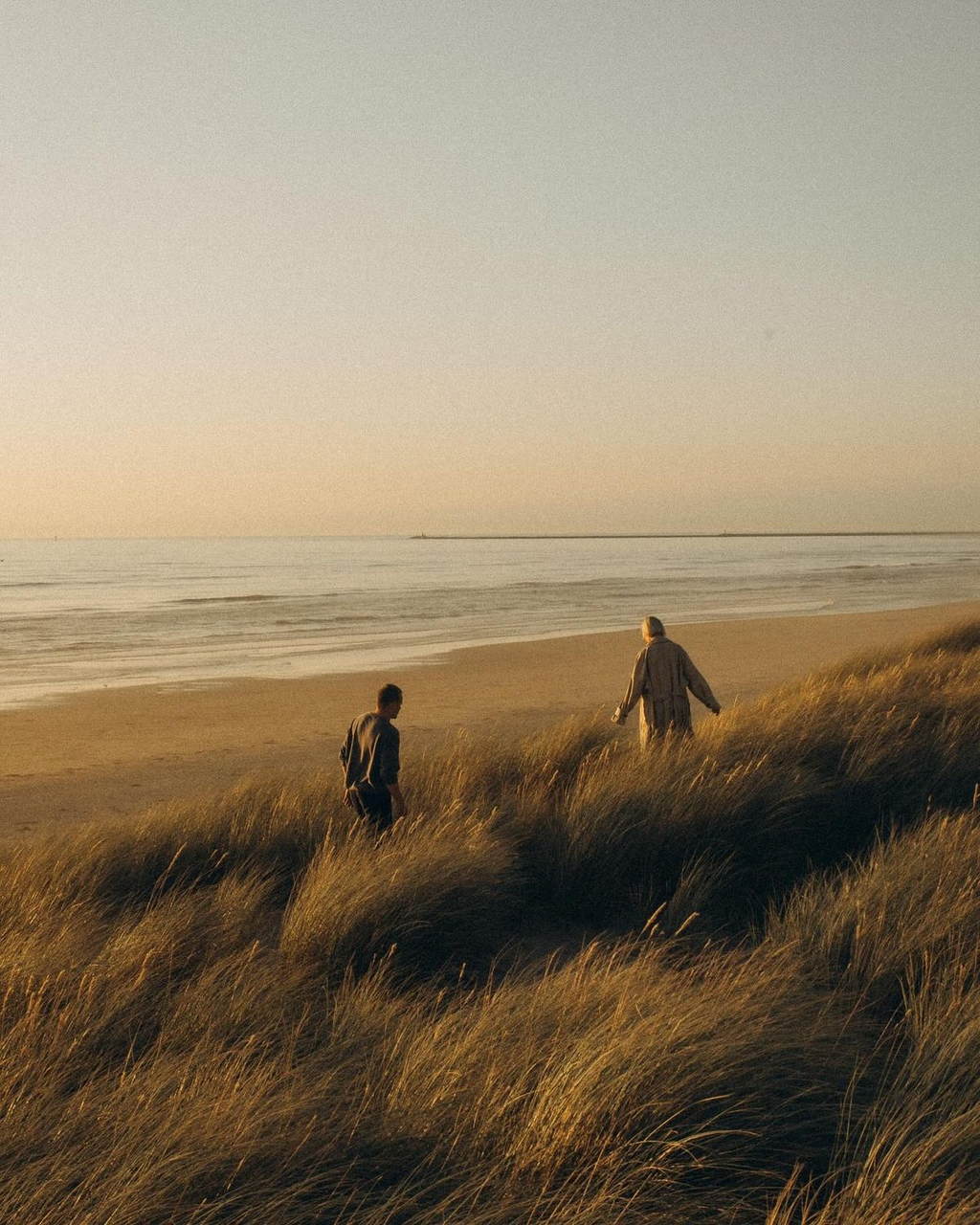 Two people walking through coastal dunes at sunset