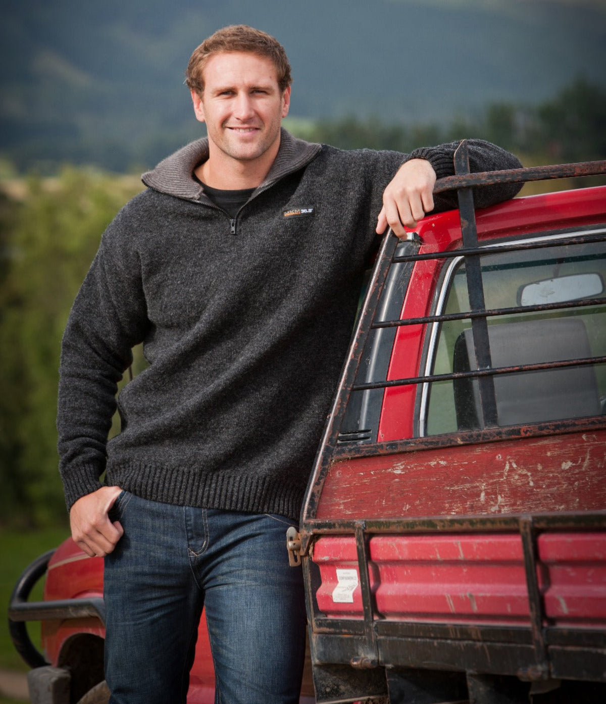 possum merino Man leaning against a red truck with mountains in the background