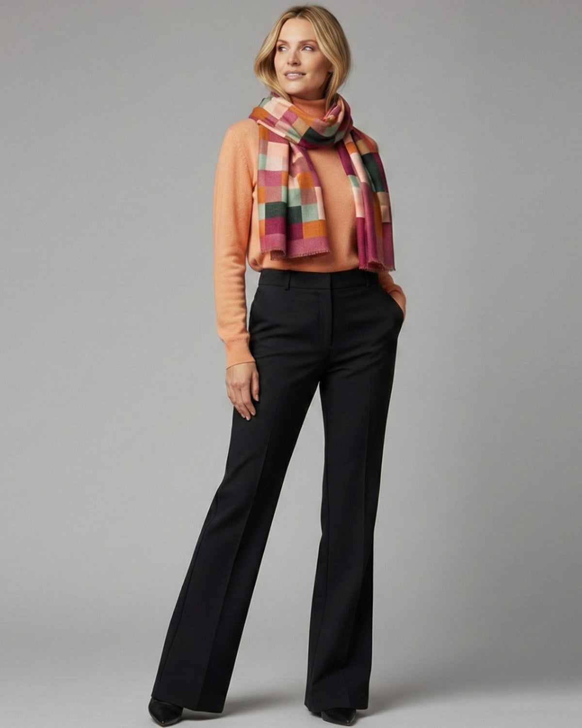 Woman wearing a merino  colorful scarf and black pants on a gray background